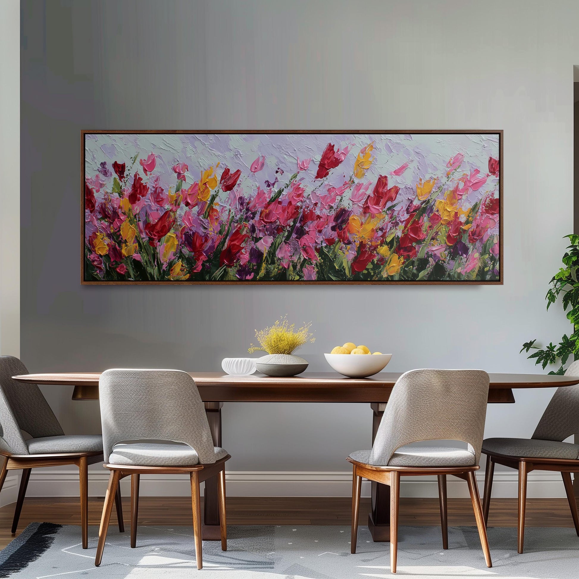 a dining room with a large painting of colorful flowers hanging on the wall above a wooden dining table with four chairs. The table is set with a bowl of fruit and a vase of flowers, creating a welcoming and cozy atmosphere.
