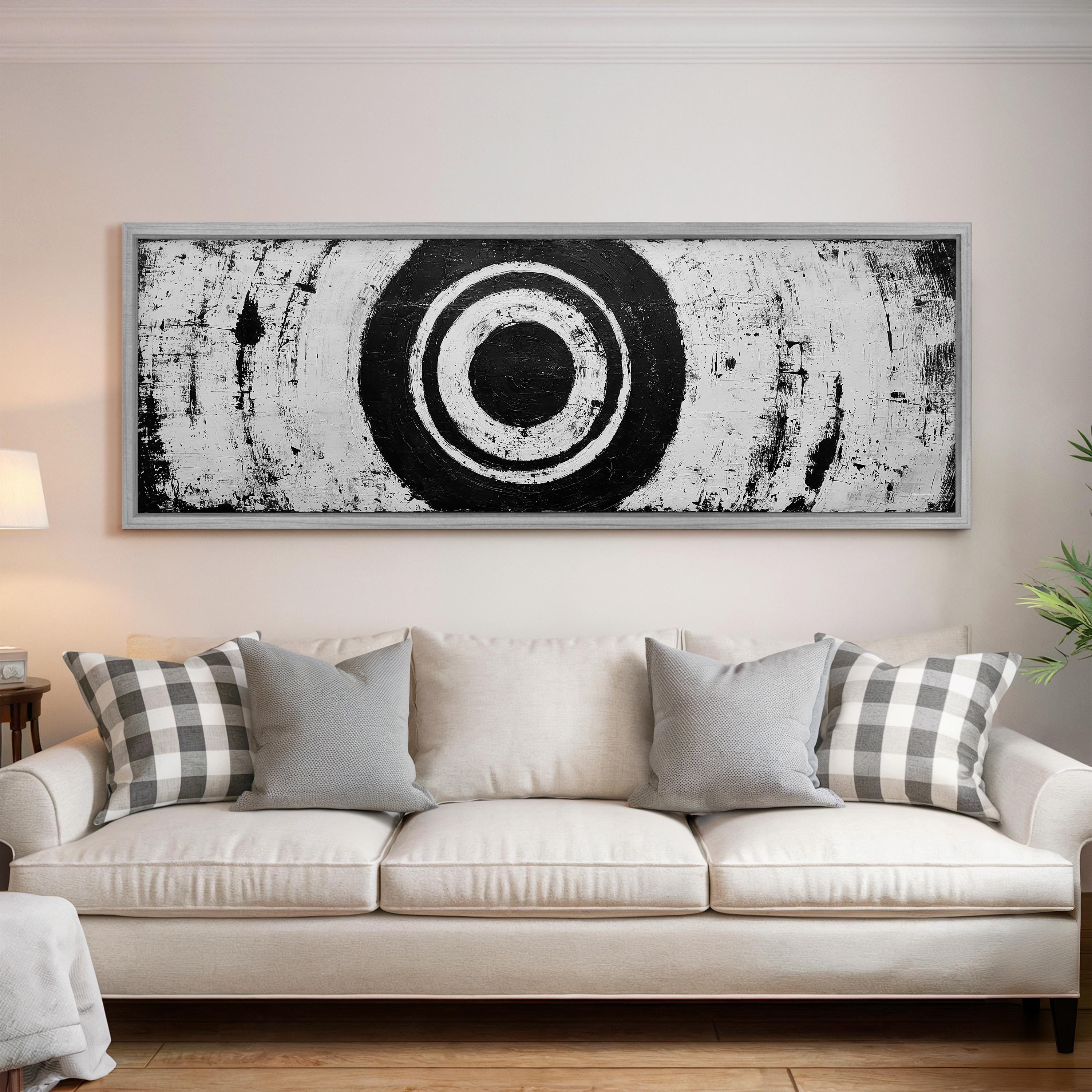 a large black and white abstract painting hanging on a wall above a white couch with gray and white plaid throw pillows.