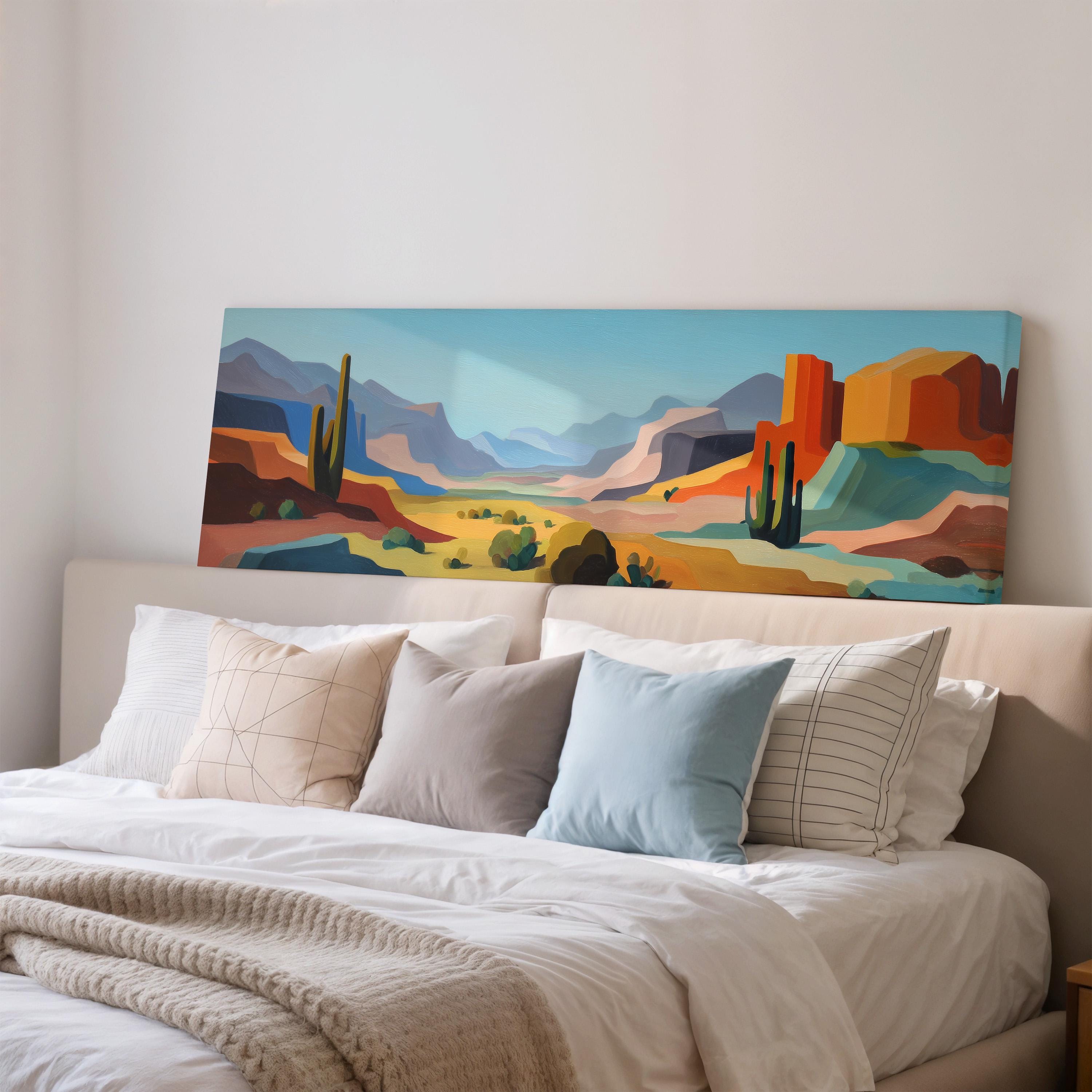 a large, colorful painting of a desert landscape hanging on a wall above a bed with white pillows and a gray blanket.