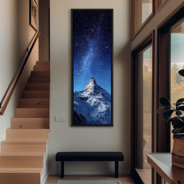 a large, framed painting of a snowy mountain peak with a starry night sky above it, hanging on the wall of a hallway.