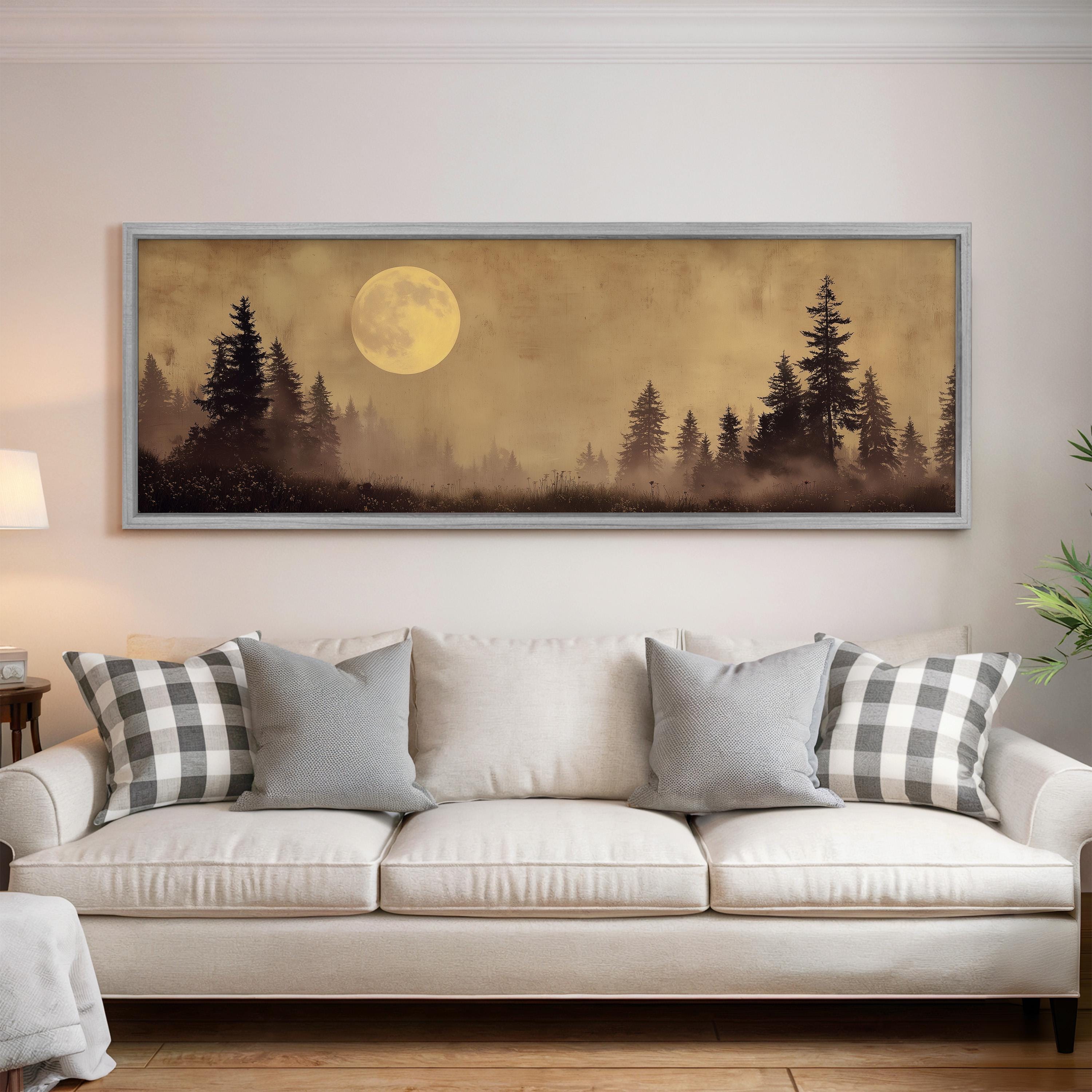 a large framed painting of a forest scene with a full moon in the background, hanging on a wall above a white sofa with patterned throw pillows.