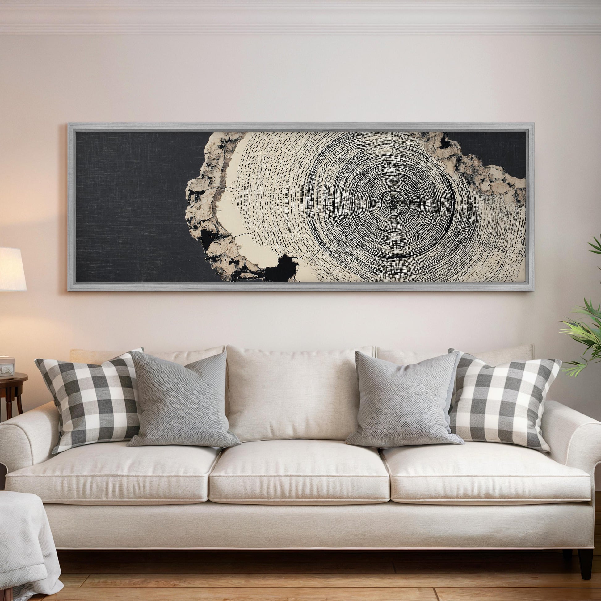 a large black and white tree trunk with concentric circles, hanging above a white couch with gray and white plaid throw pillows.