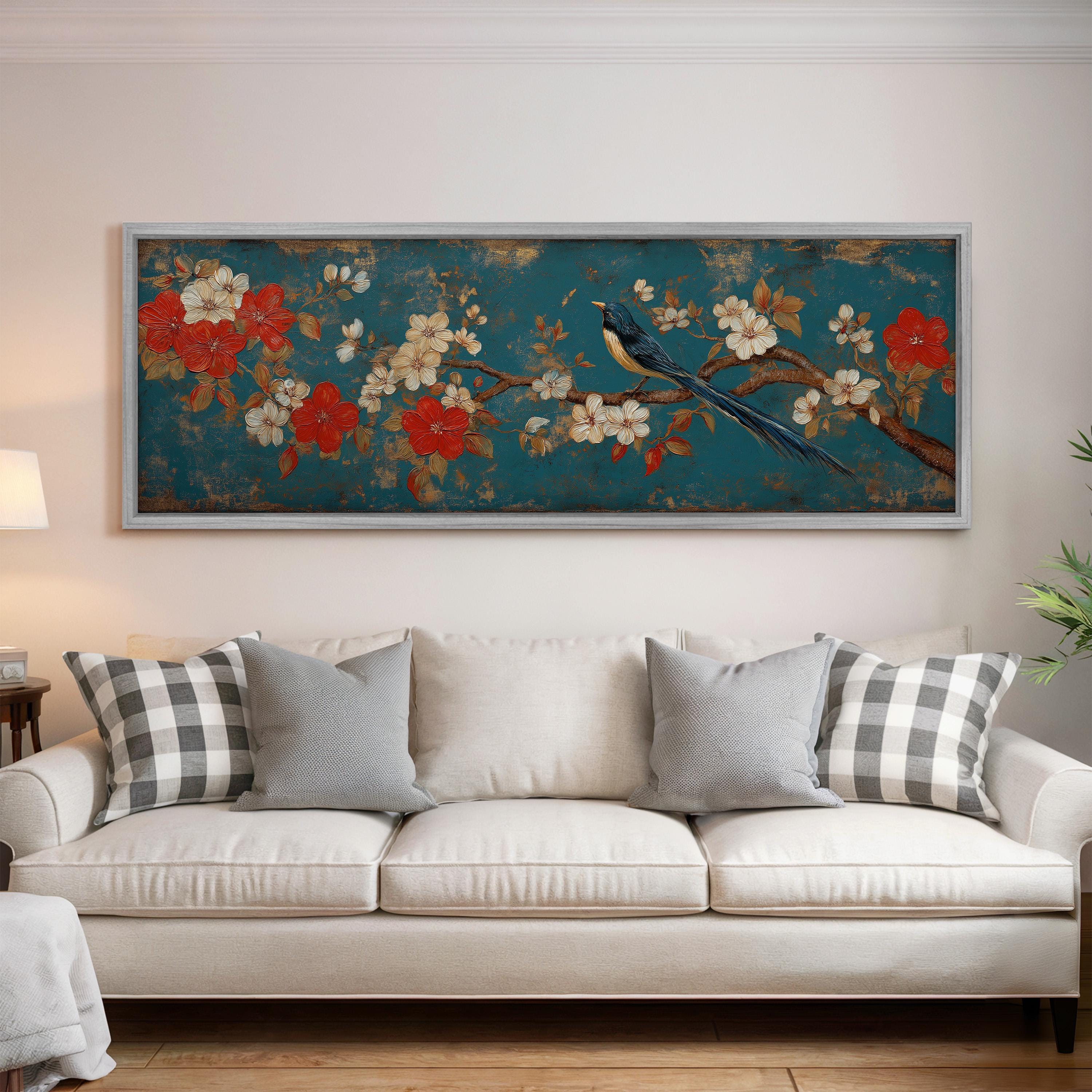 a large, framed painting of a bird perched on a branch with flowers, hanging on a wall above a white couch with gray and white plaid throw pillows.