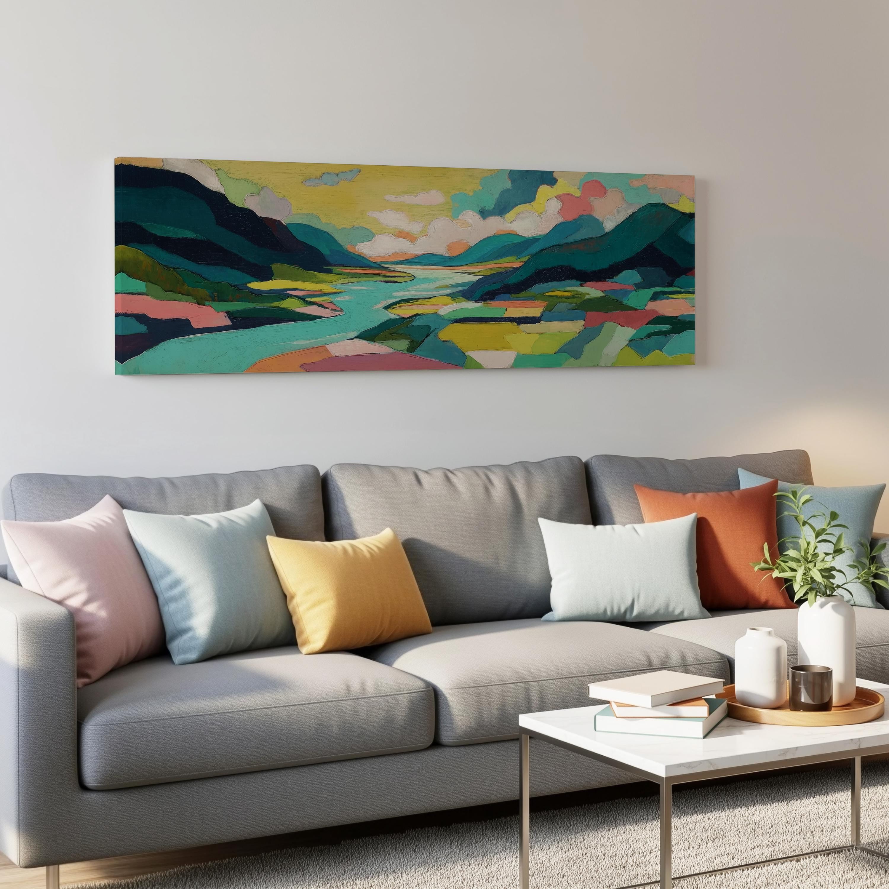 a modern living room with a gray sofa adorned with colorful throw pillows. Above the sofa, a large landscape painting depicting a serene mountain scene is displayed on the wall. The room also includes a coffee table with books and a plant, creating a cozy and inviting atmosphere.