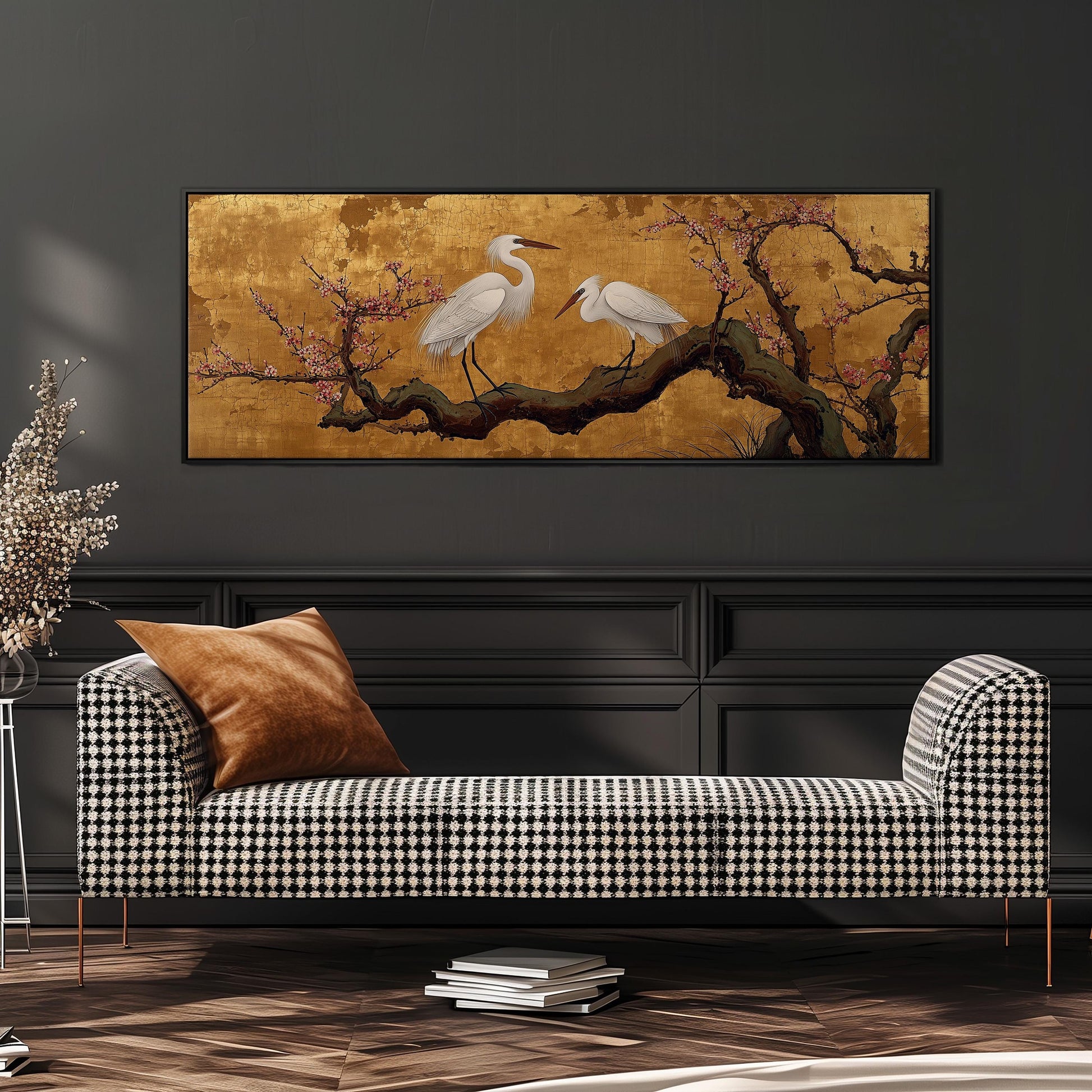 a black and white checkered sofa with a brown throw pillow, set against a dark wall with a large framed painting of two white birds perched on a branch with pink flowers above it.