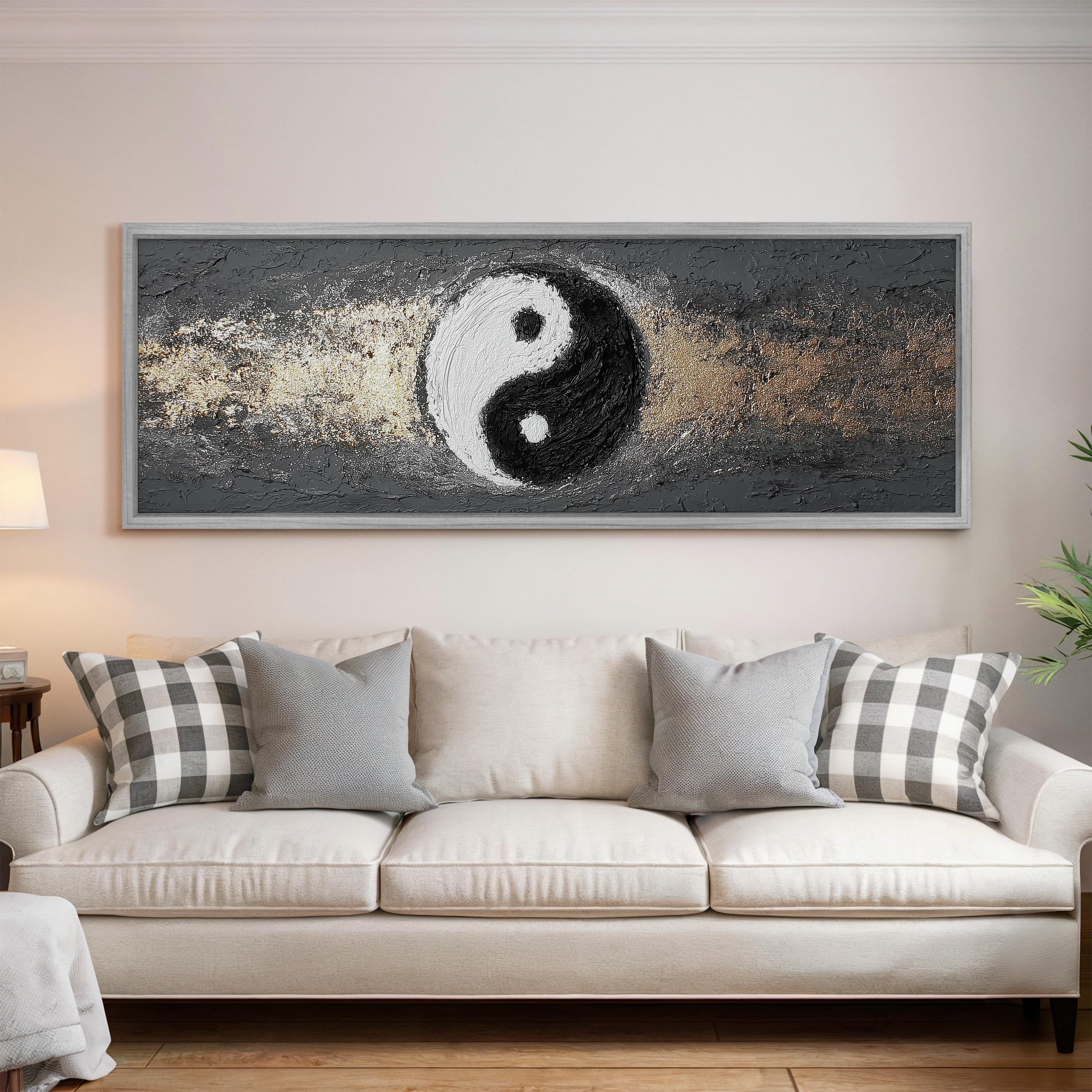 a large, framed painting of a yin and yang symbol hanging on a wall above a white couch with gray and white plaid throw pillows.