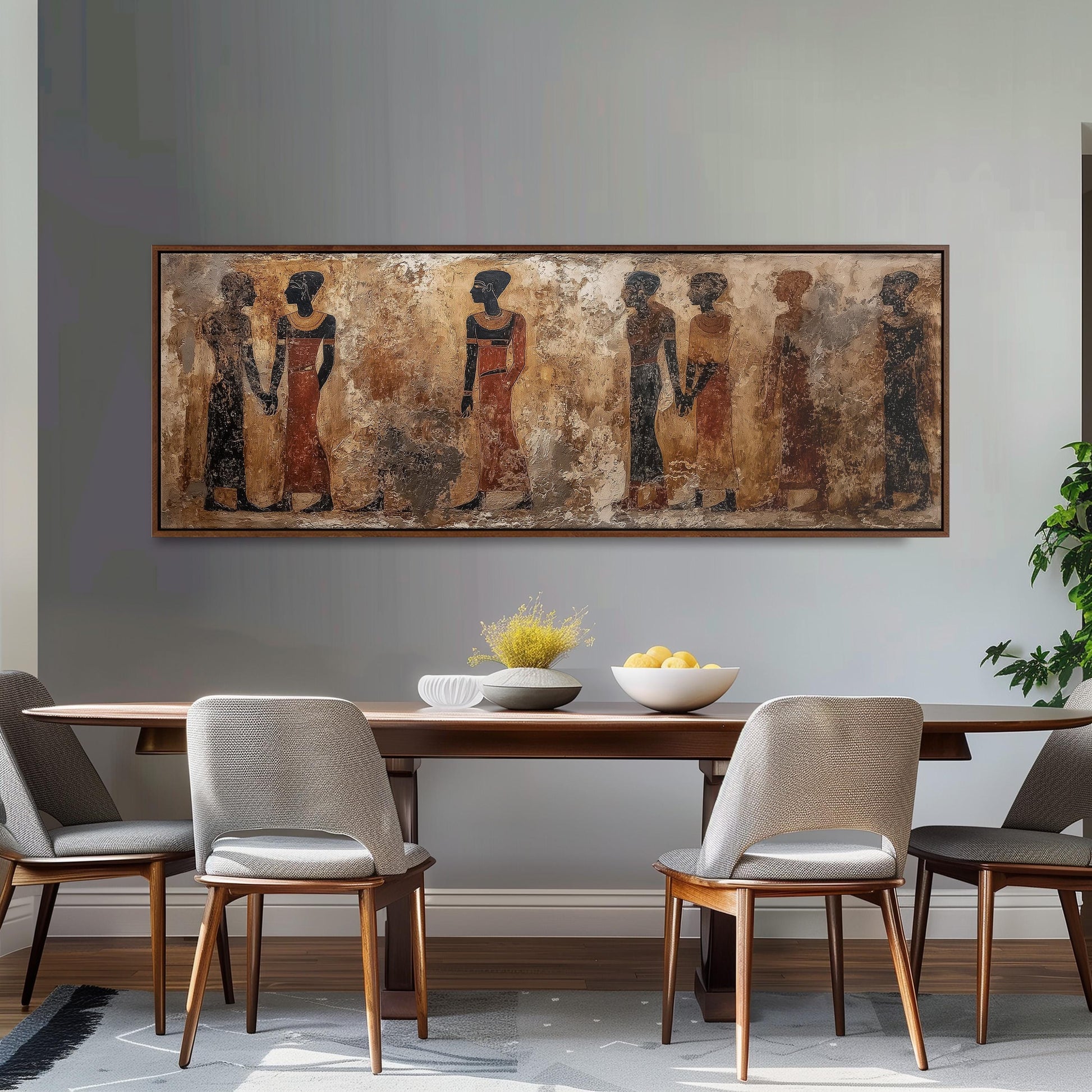 a dining room with a large painting of ancient Egyptian women hanging on the wall above a wooden dining table with four chairs. The table is set with a bowl of fruit and a vase of flowers, creating a warm and inviting atmosphere.
