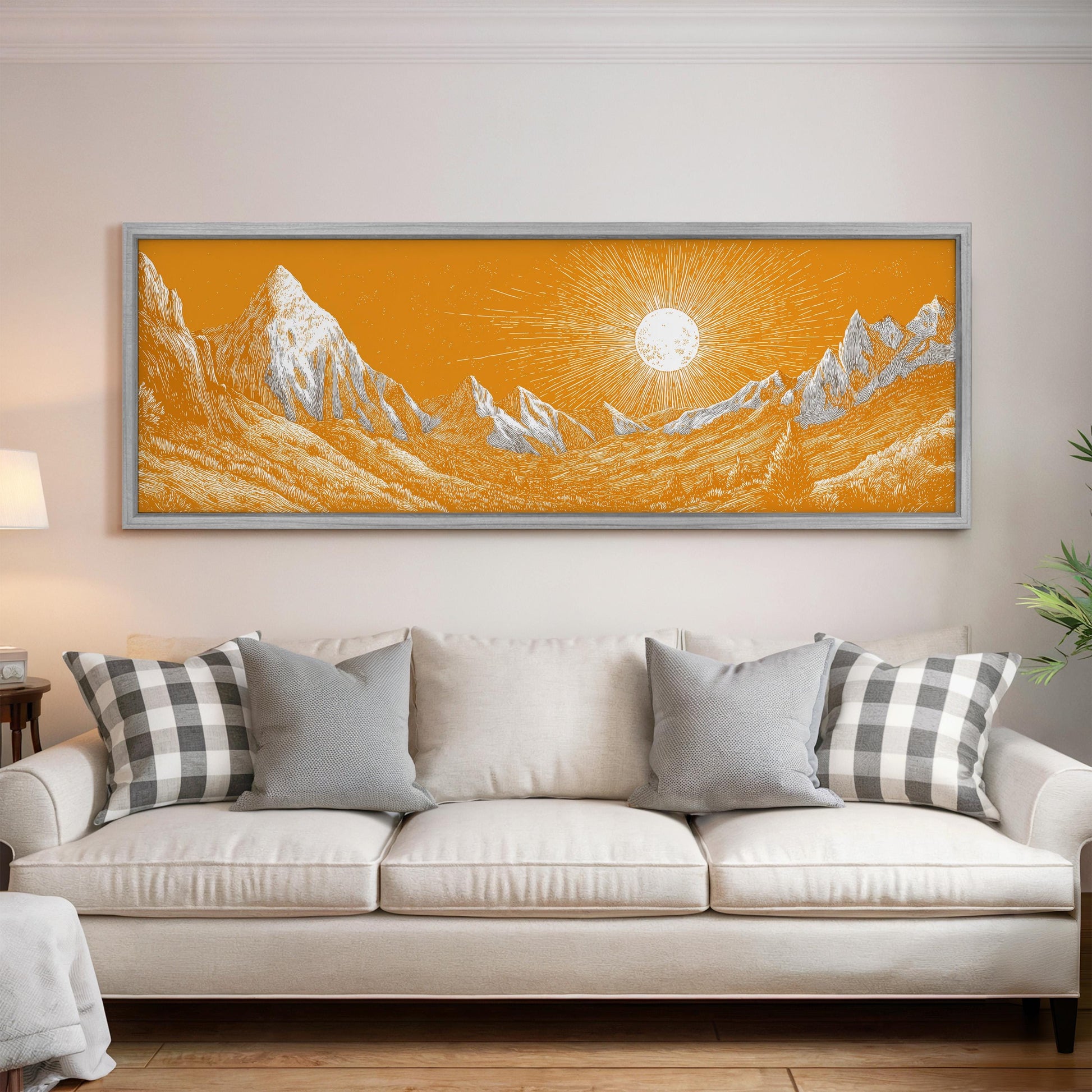 a large, framed painting of a mountain landscape with a sun in the background, hanging on a wall above a white couch with gray and white plaid throw pillows.