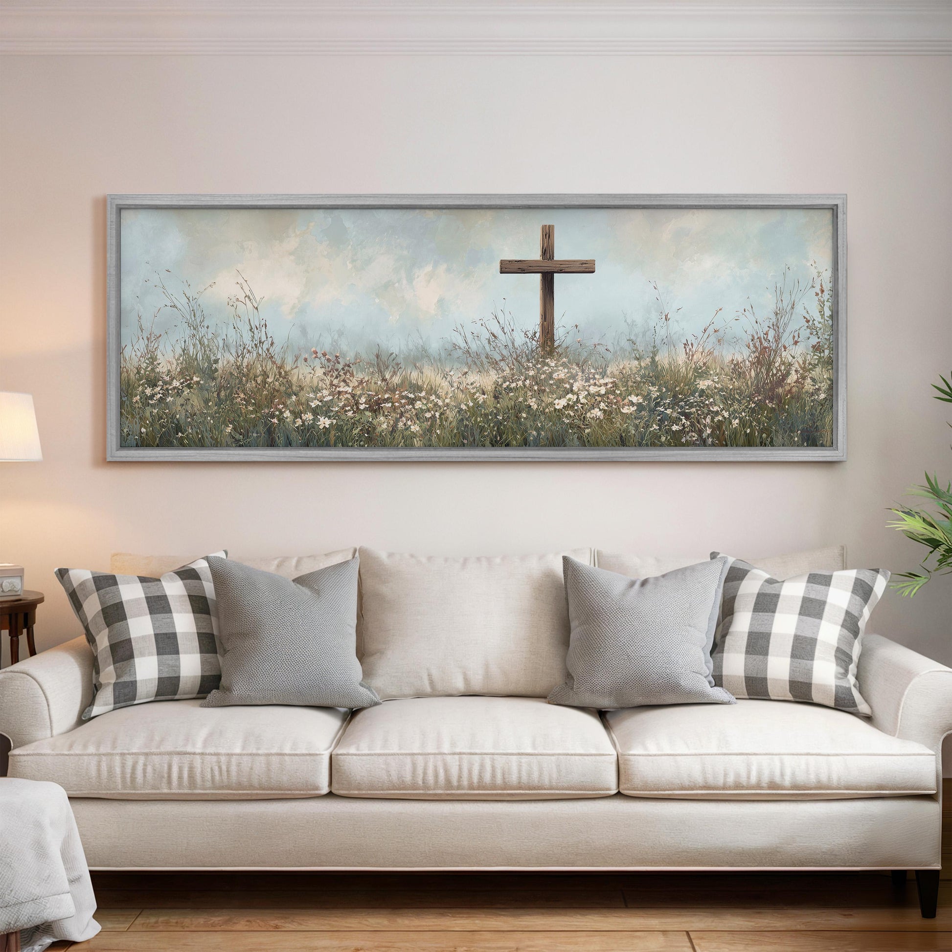 a large painting of a cross in a field of flowers hanging on a wall above a white couch with gray and white pillows.