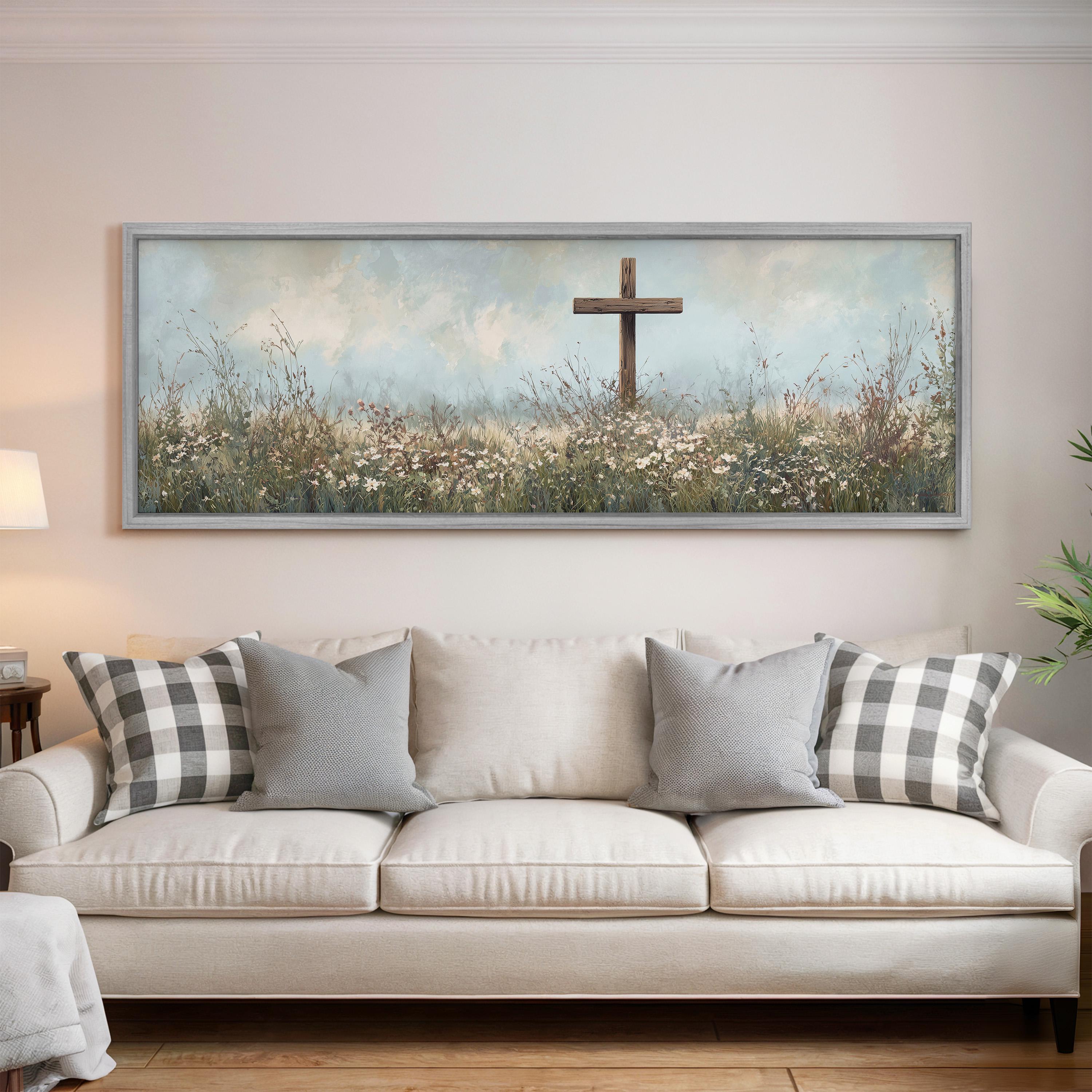 a large painting of a cross in a field of flowers hanging on a wall above a white couch with gray and white pillows.