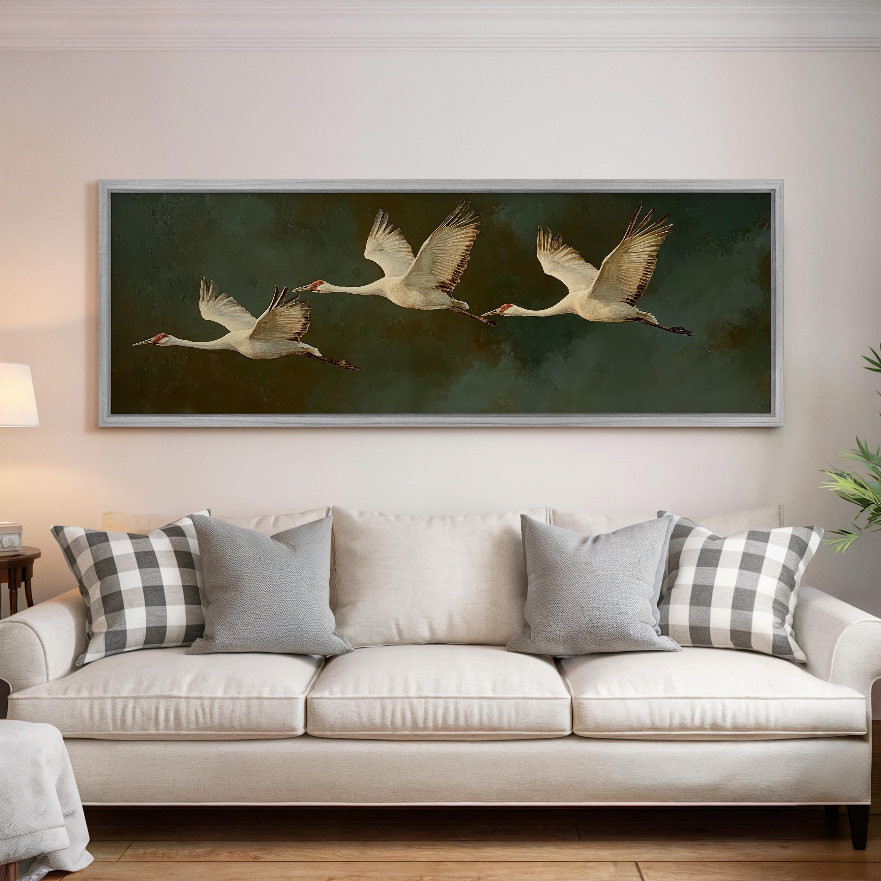 a large painting of three white birds in flight, hanging on a wall above a white sofa with gray and white patterned throw pillows.