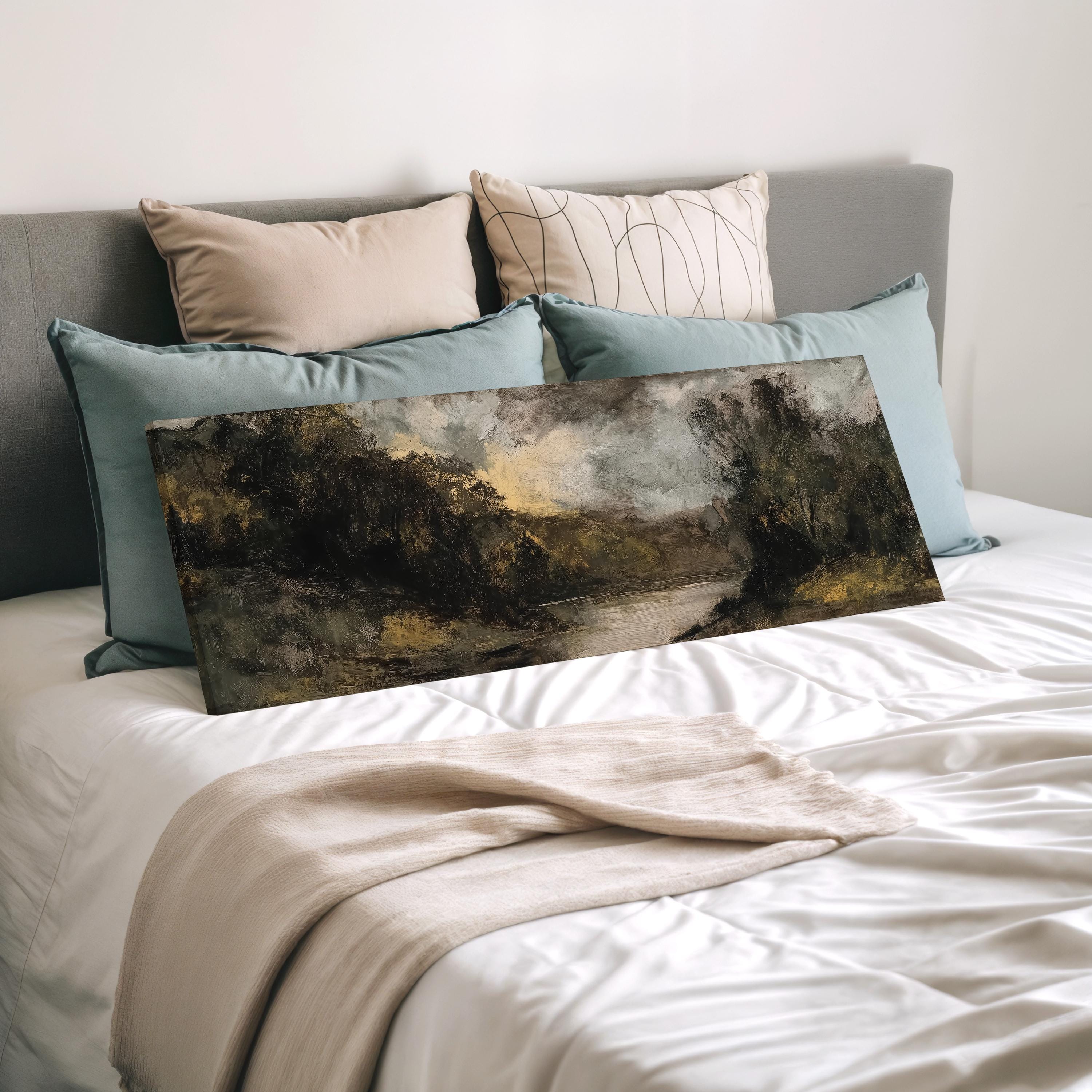 a bedroom with a bed covered in white sheets and a painting of a landscape on the bed. The painting is surrounded by multiple pillows, creating a cozy and inviting atmosphere.