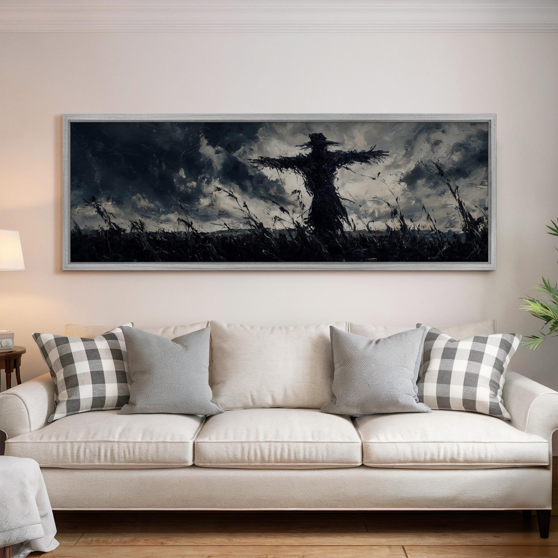 a large black and white painting of a scarecrow on a field, hanging on a wall above a white couch with gray and white plaid throw pillows.