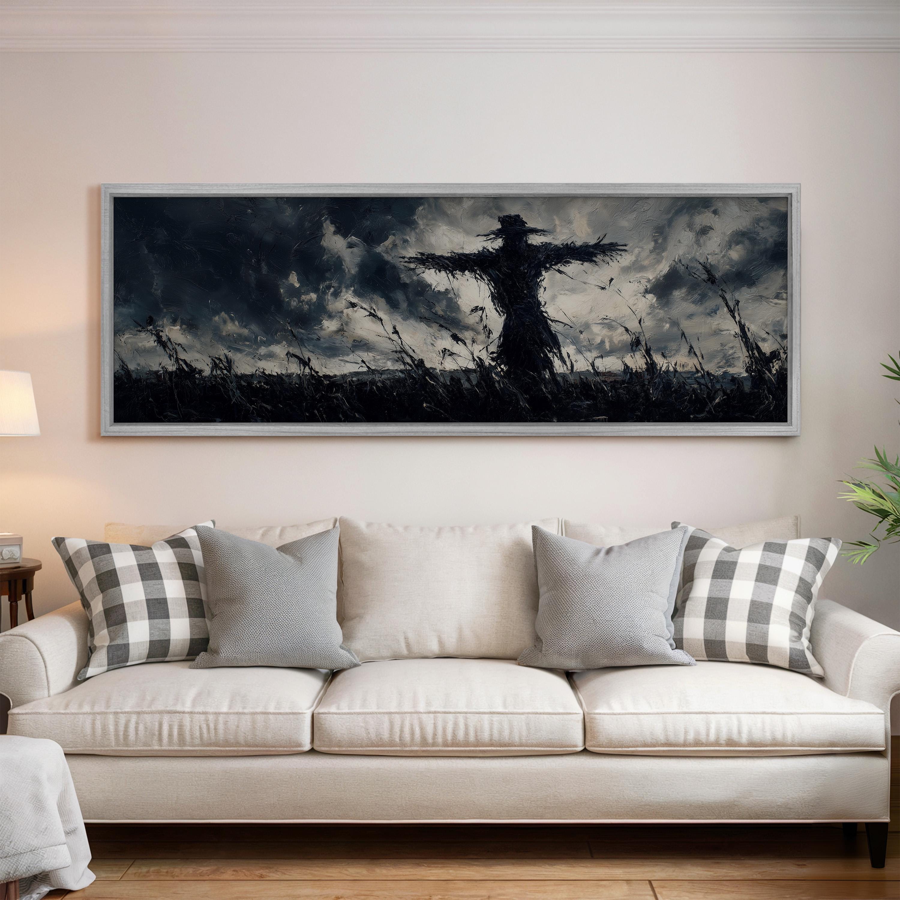 a large black and white painting of a scarecrow on a field, hanging on a wall above a white couch with gray and white plaid throw pillows.