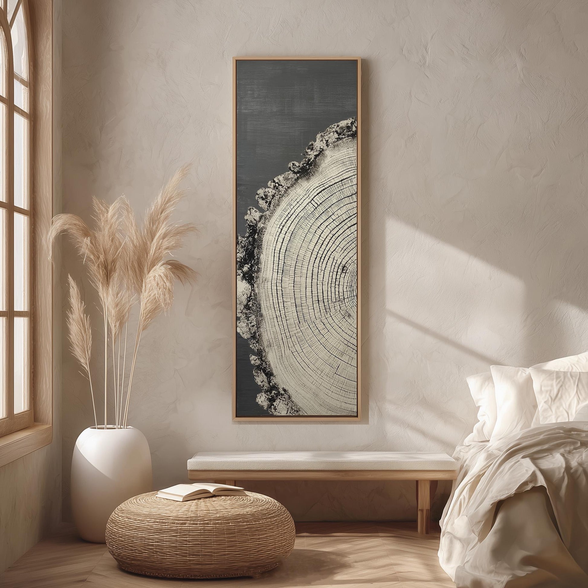 a serene and minimalist bedroom interior with a large window, a wooden bench, a woven ottoman, and a framed artwork featuring a tree trunk on the wall.