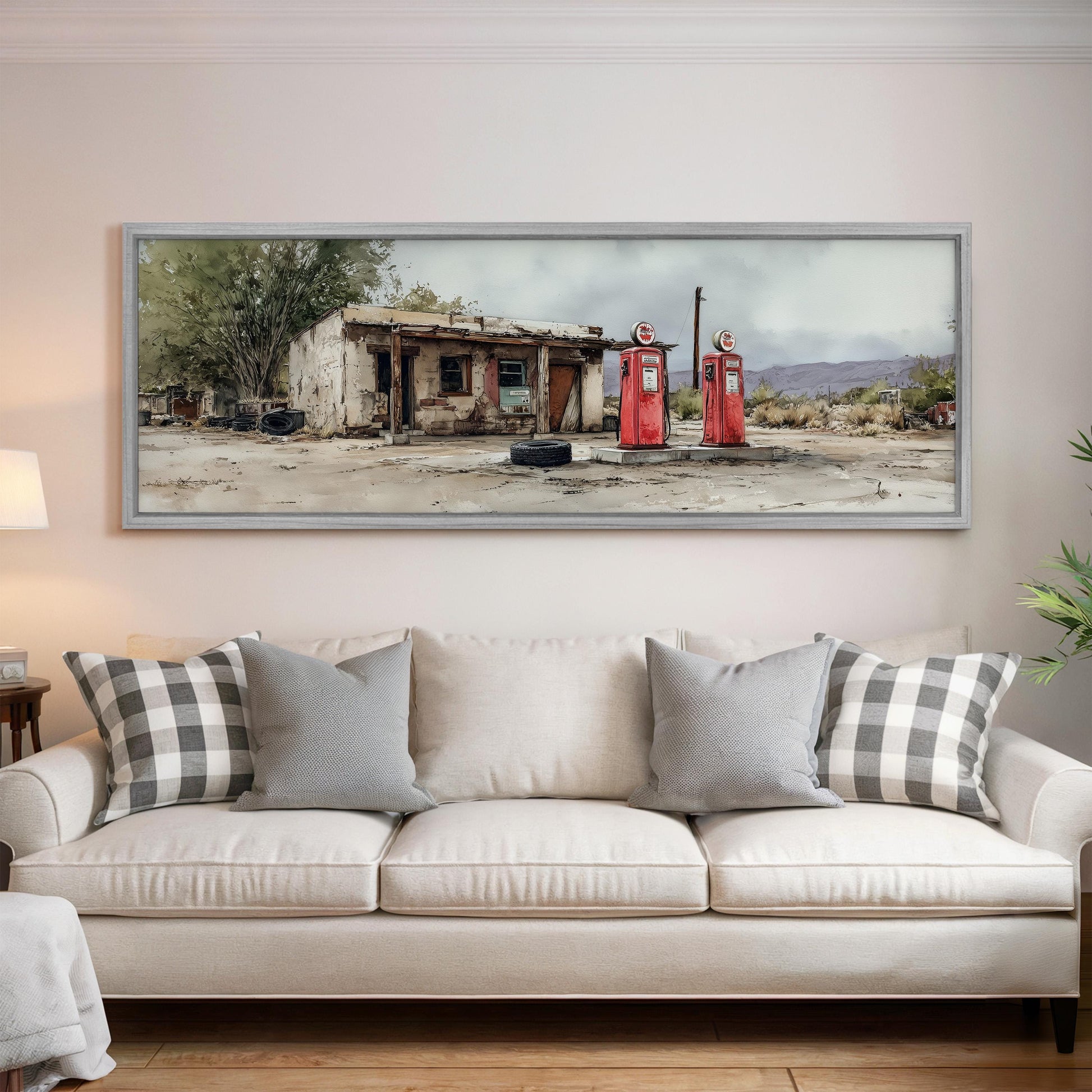 a large framed painting of a dilapidated building with two red gas pumps in front of it, set against a cloudy sky.