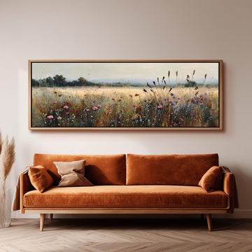 a large, framed painting of a field with flowers hanging on a wall above a brown sofa.