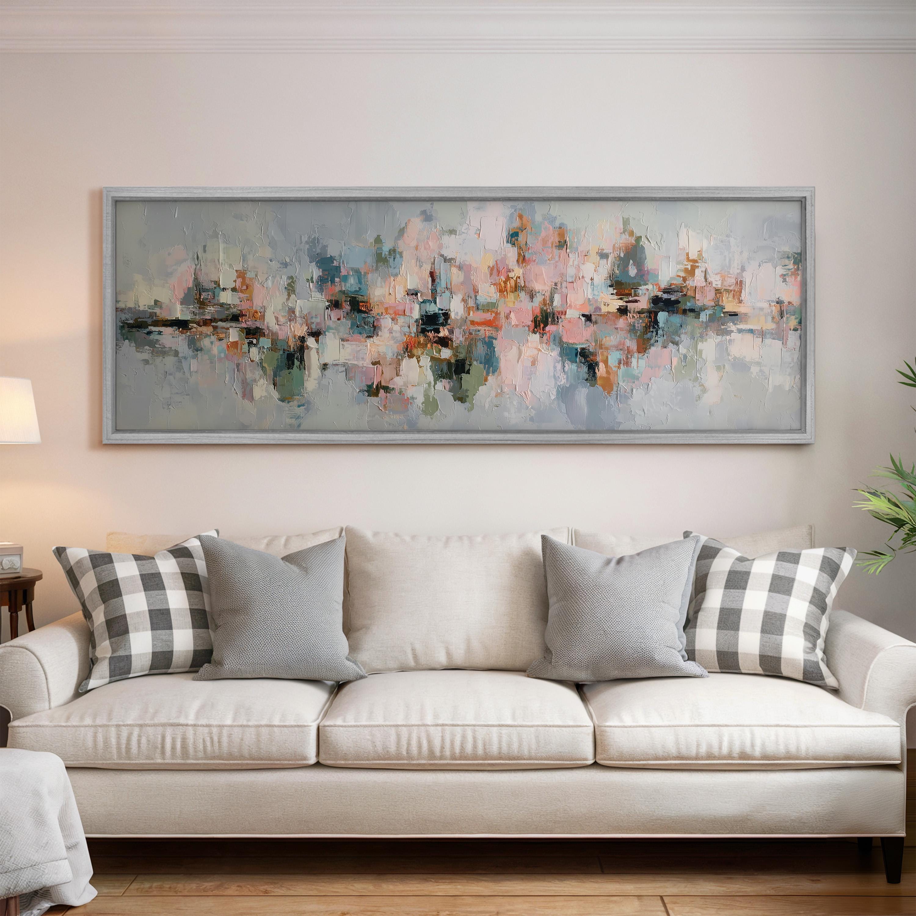 a large, abstract painting hanging on a wall above a white sofa with gray and black plaid throw pillows.