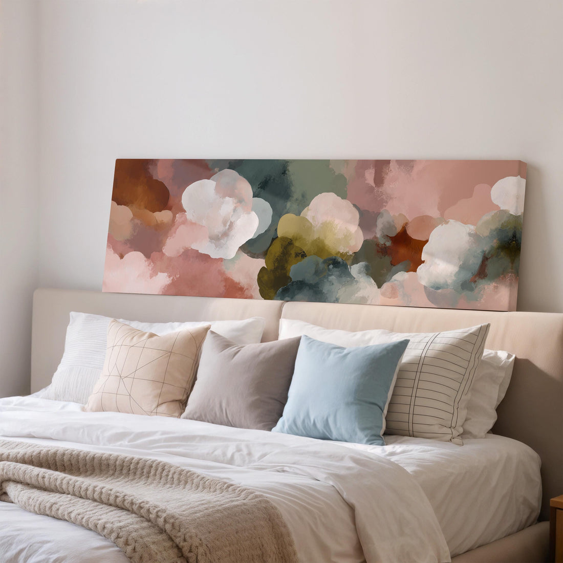 a large bed with a white comforter and a variety of colorful pillows. Above the bed, there is a large canvas print depicting a vibrant abstract painting of clouds in different colors.