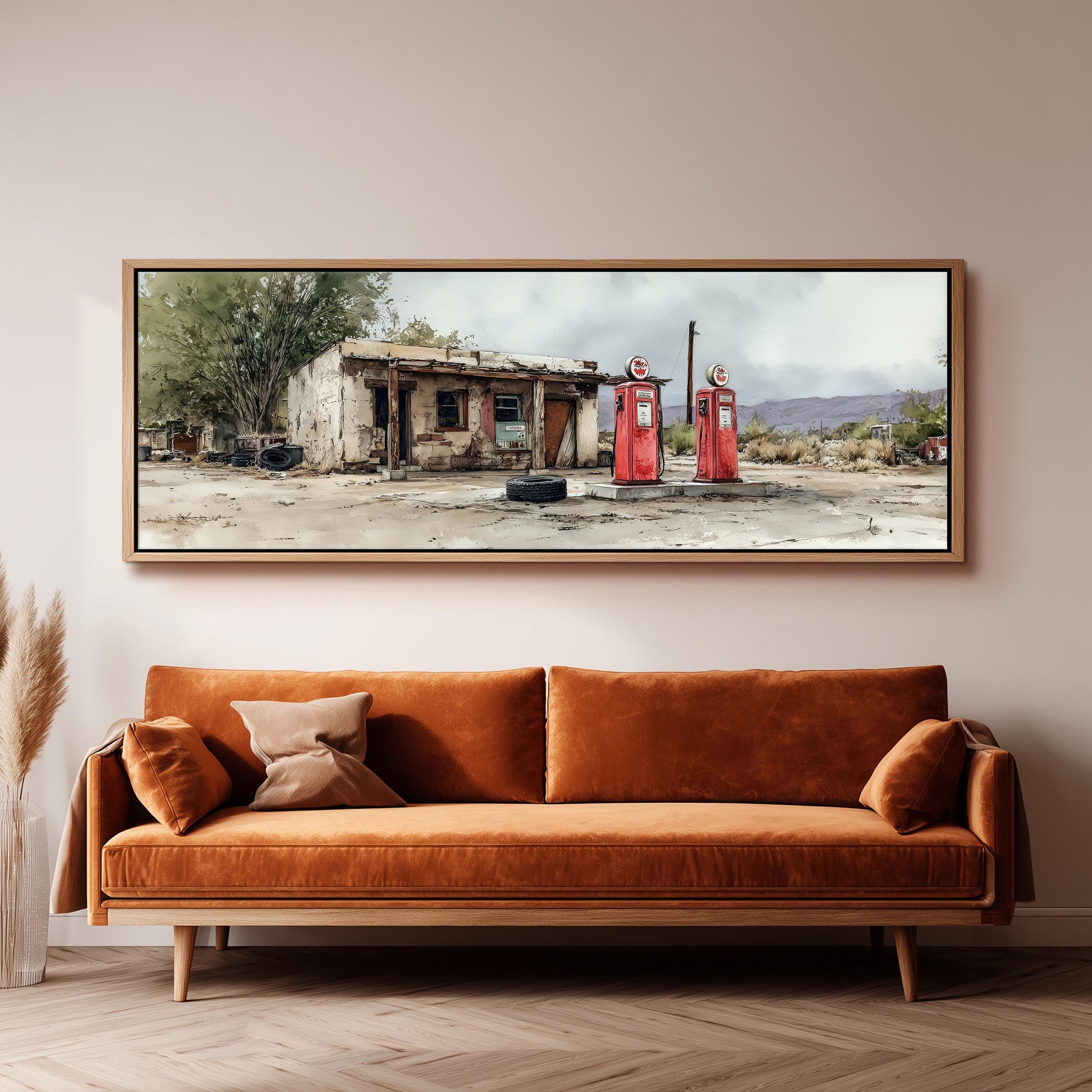 a large, framed painting of a dilapidated building with two red gas pumps in front of it, hanging on a wall above a brown sofa.