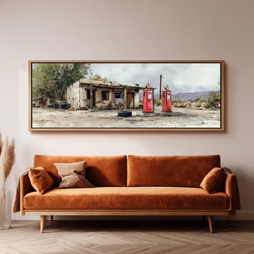 a large, framed painting of a dilapidated building with two red gas pumps in front of it, hanging on a wall above a brown sofa.
