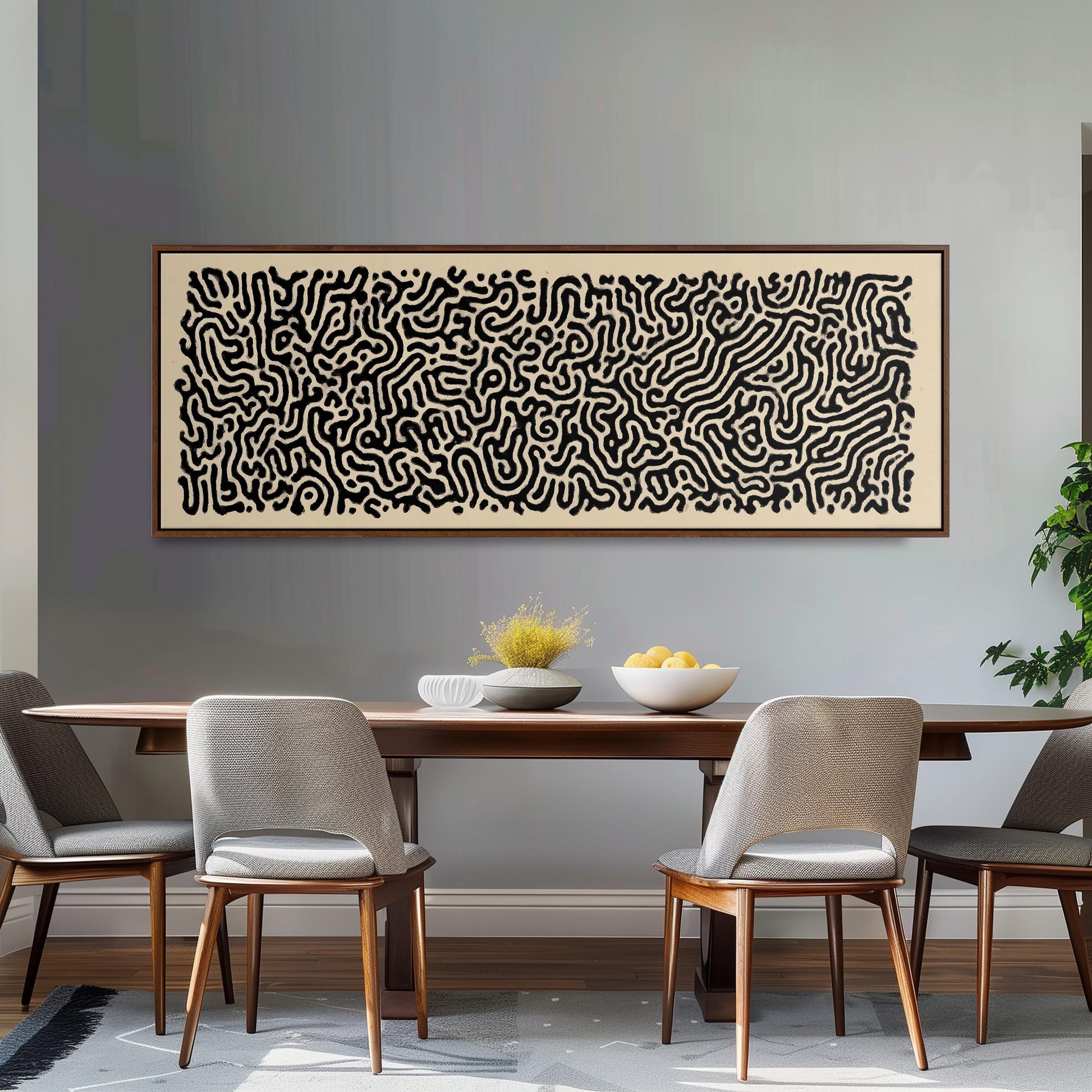 a dining room with a wooden table and four chairs. Above the table, there is a large abstract painting with a black and white color scheme. The table is set with a bowl of fruit and a vase of flowers, creating a cozy and inviting atmosphere.