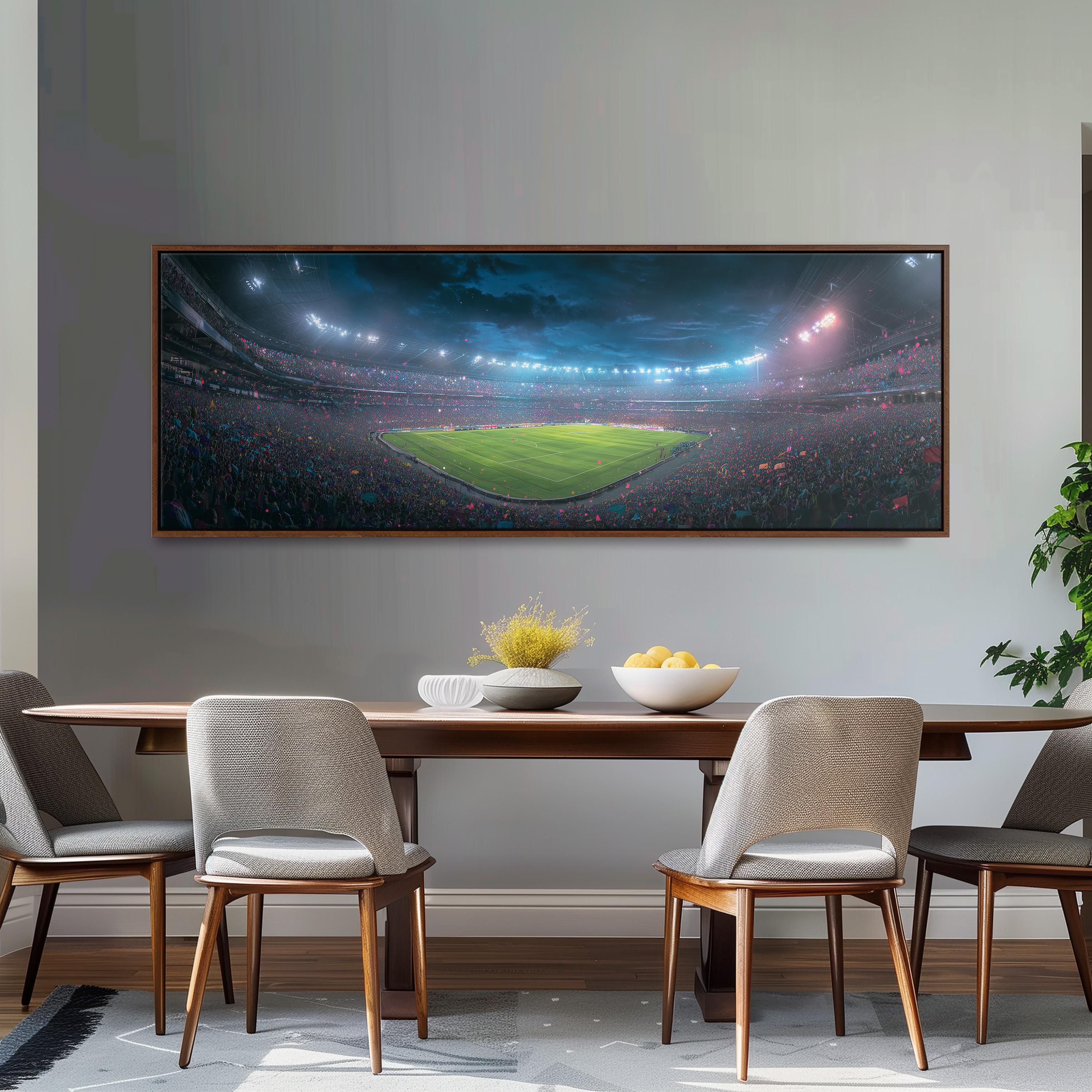a large framed picture of a soccer stadium with a crowd of spectators, hanging on a wall above a wooden dining table with four chairs.