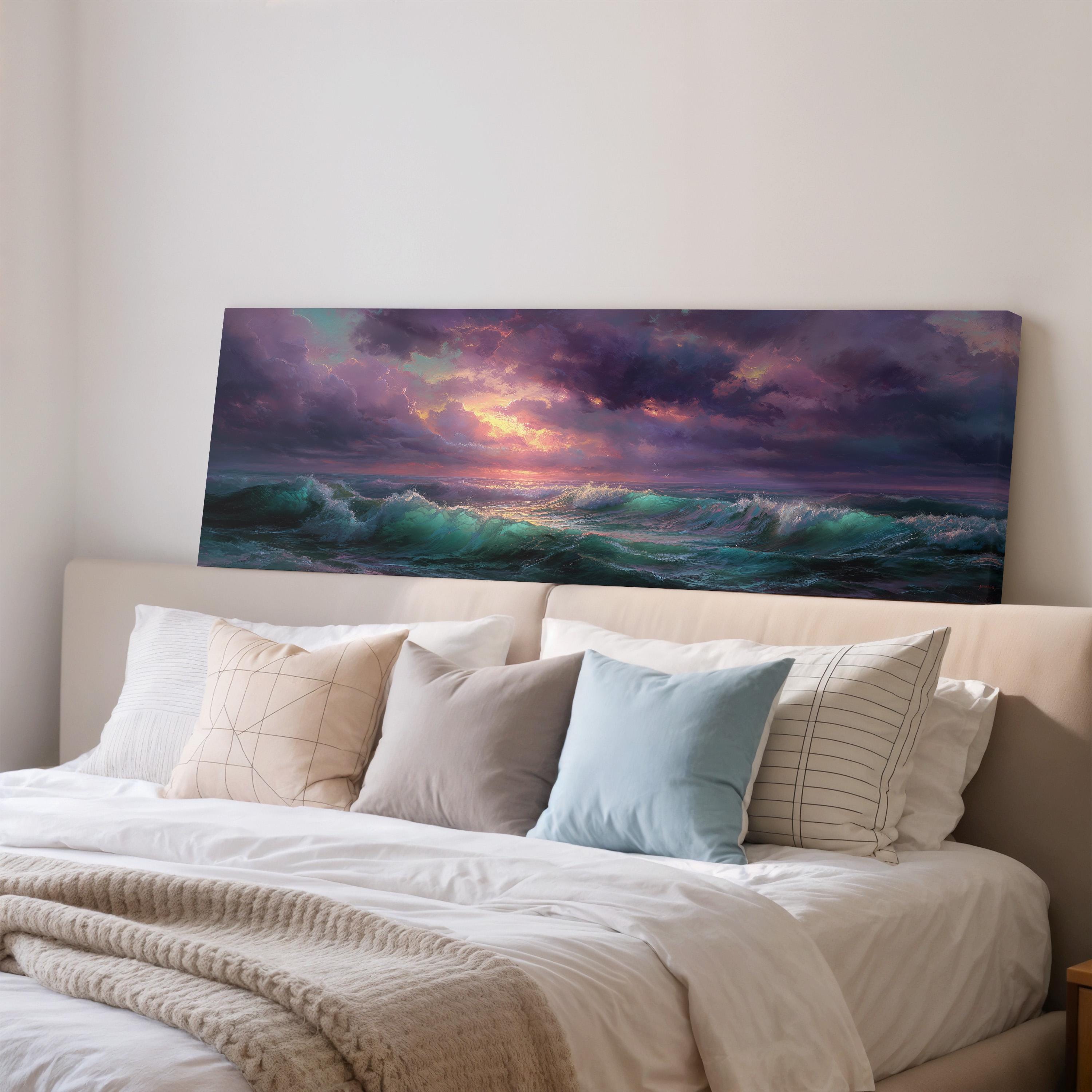 a large painting of a sunset over the ocean, hanging on a wall above a bed with white pillows and a gray blanket.