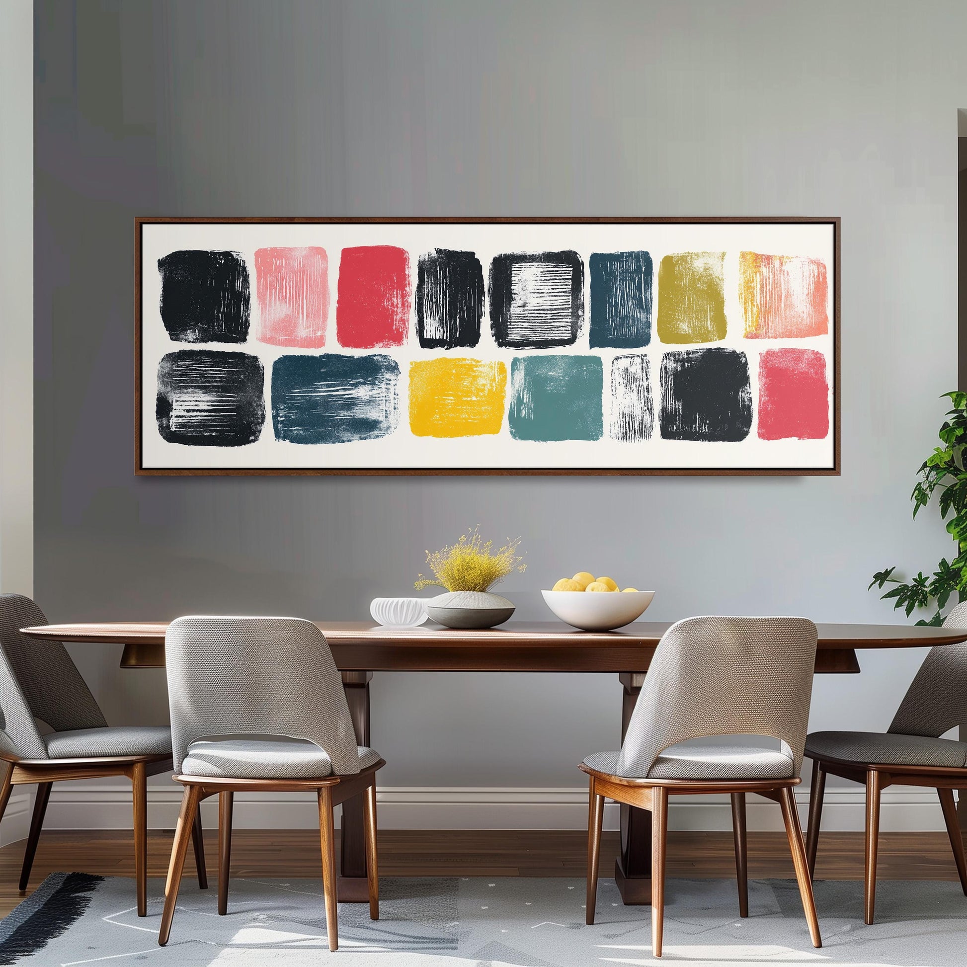 a modern dining room with a wooden table and four chairs. Above the table, there is a large abstract painting with various colored squares. The table is set with a bowl of fruit and a vase of flowers, creating a welcoming and stylish atmosphere.