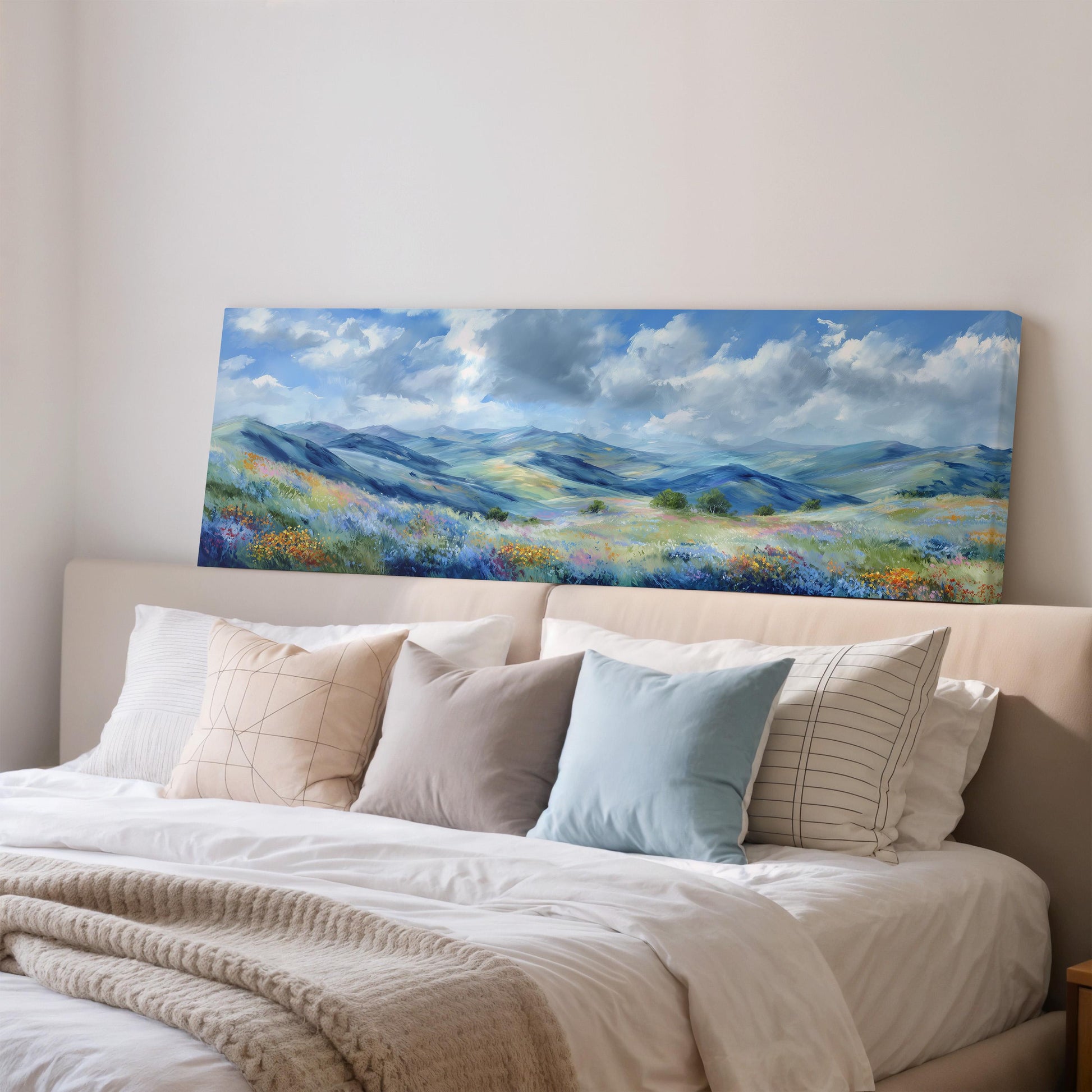 a large landscape painting hanging on a wall above a bed with white pillows and a gray blanket.