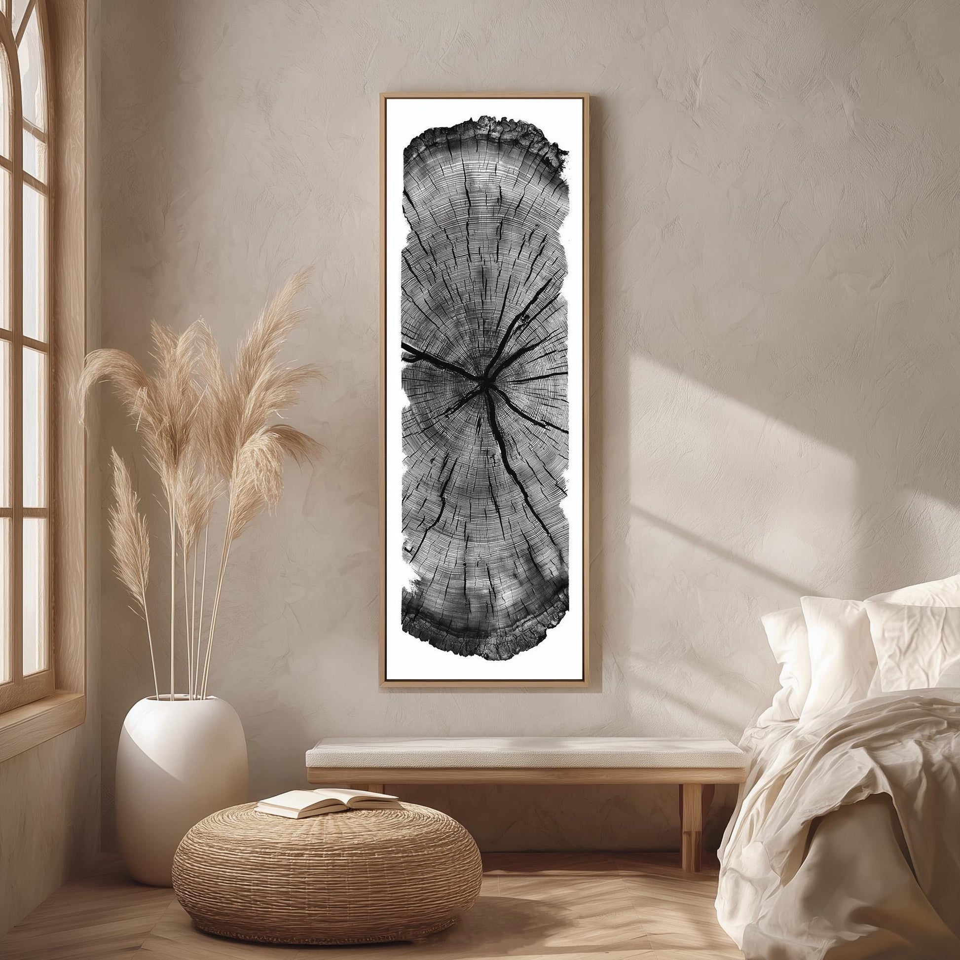 a minimalist bedroom setting with a large black and white tree trunk print hanging on the wall, a white bed with a white pillow, a white vase with potted plants, and a woven ottoman.
