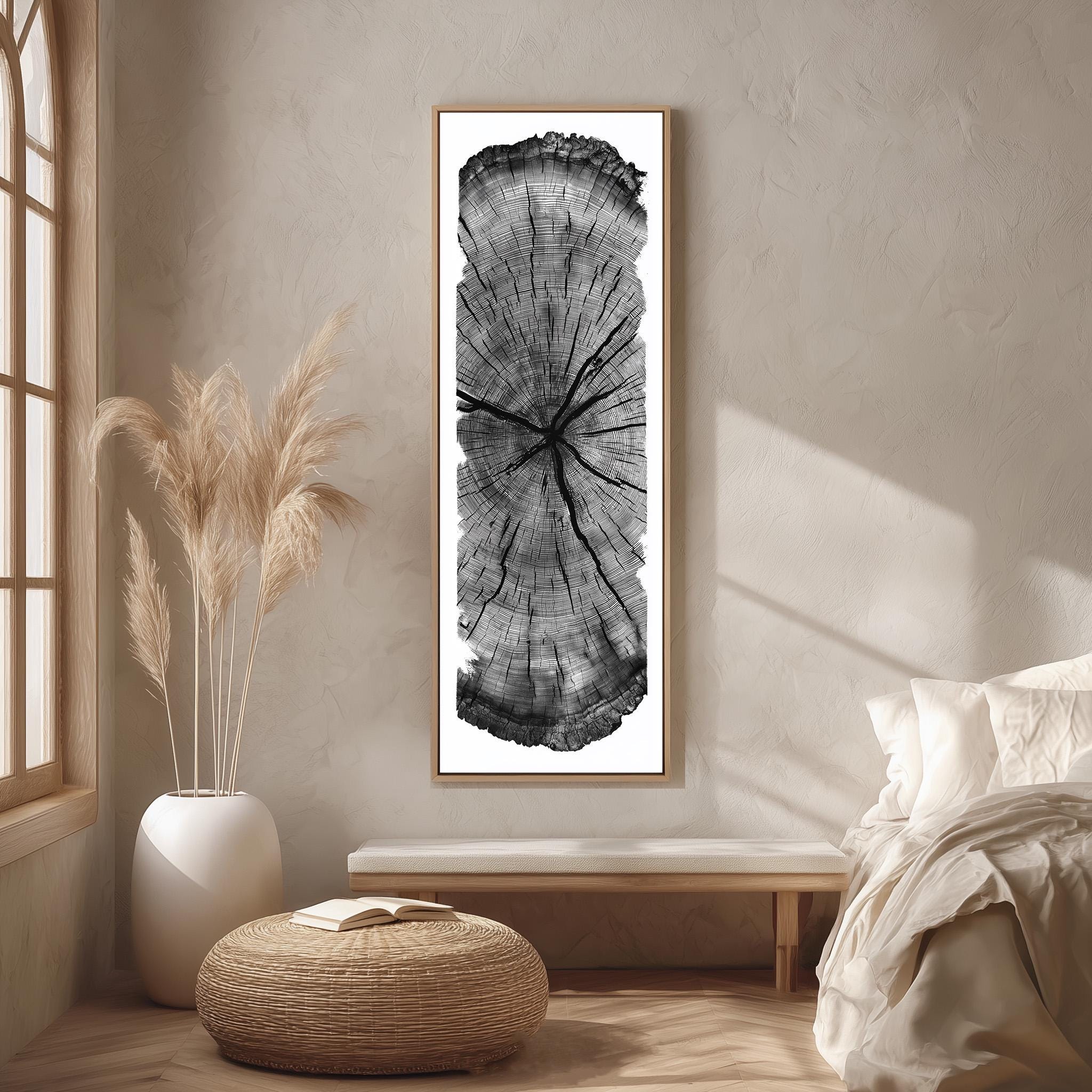 a minimalist bedroom setting with a large black and white tree trunk print hanging on the wall, a white bed with a white pillow, a white vase with potted plants, and a woven ottoman.