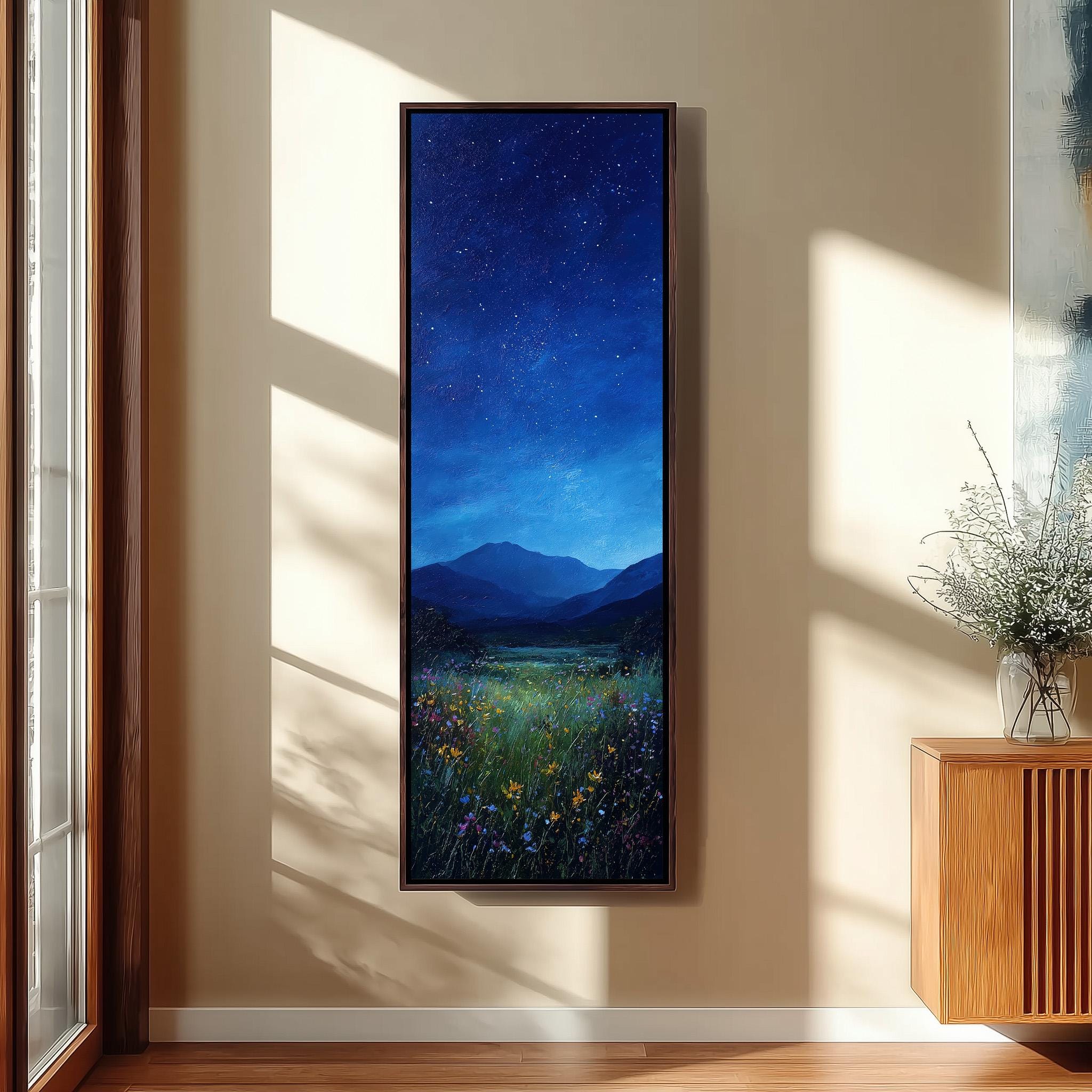 a large framed painting of a serene landscape with a starry night sky, mountains, and a field of flowers.