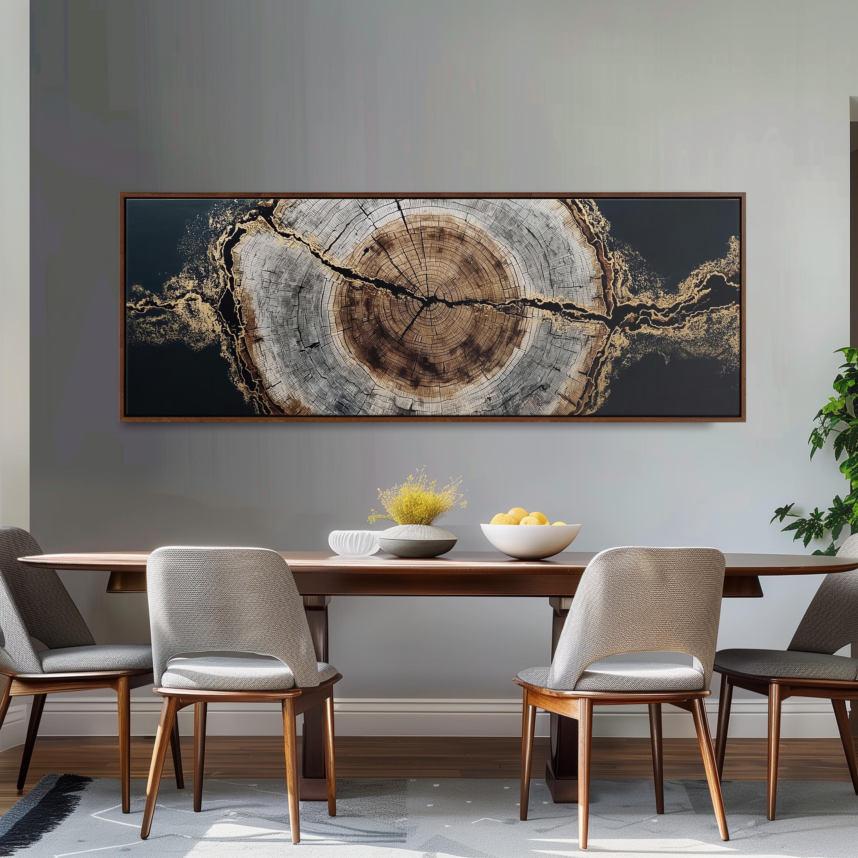 a dining room with a large wooden table and four matching chairs. Above the table, there is a large framed artwork depicting a tree trunk with a circular design. The table is set with a bowl of fruit and a vase of flowers, creating a cozy and inviting atmosphere.