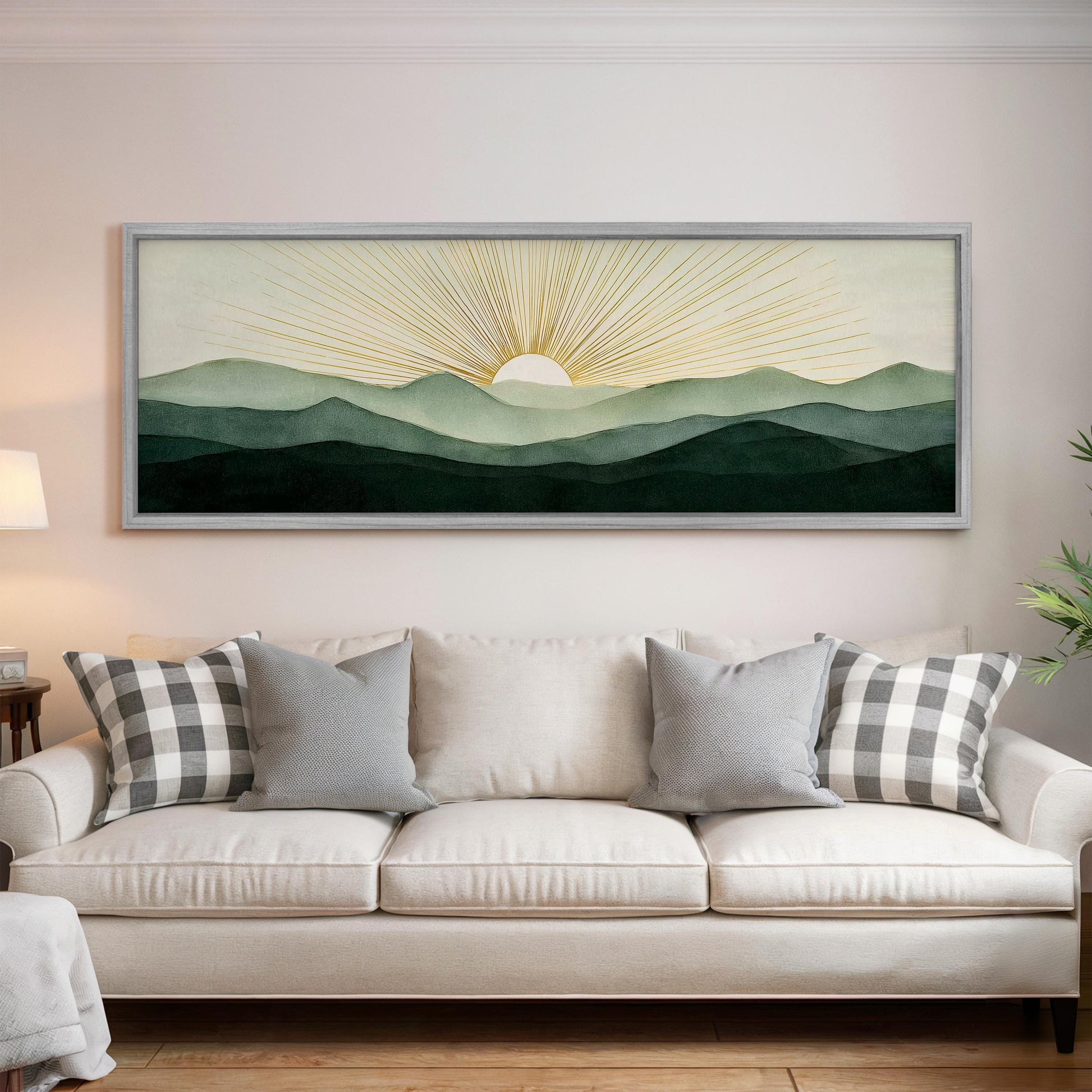 a large framed painting of a sunrise over a mountain landscape, hanging on a wall above a white sofa with gray and white patterned pillows.