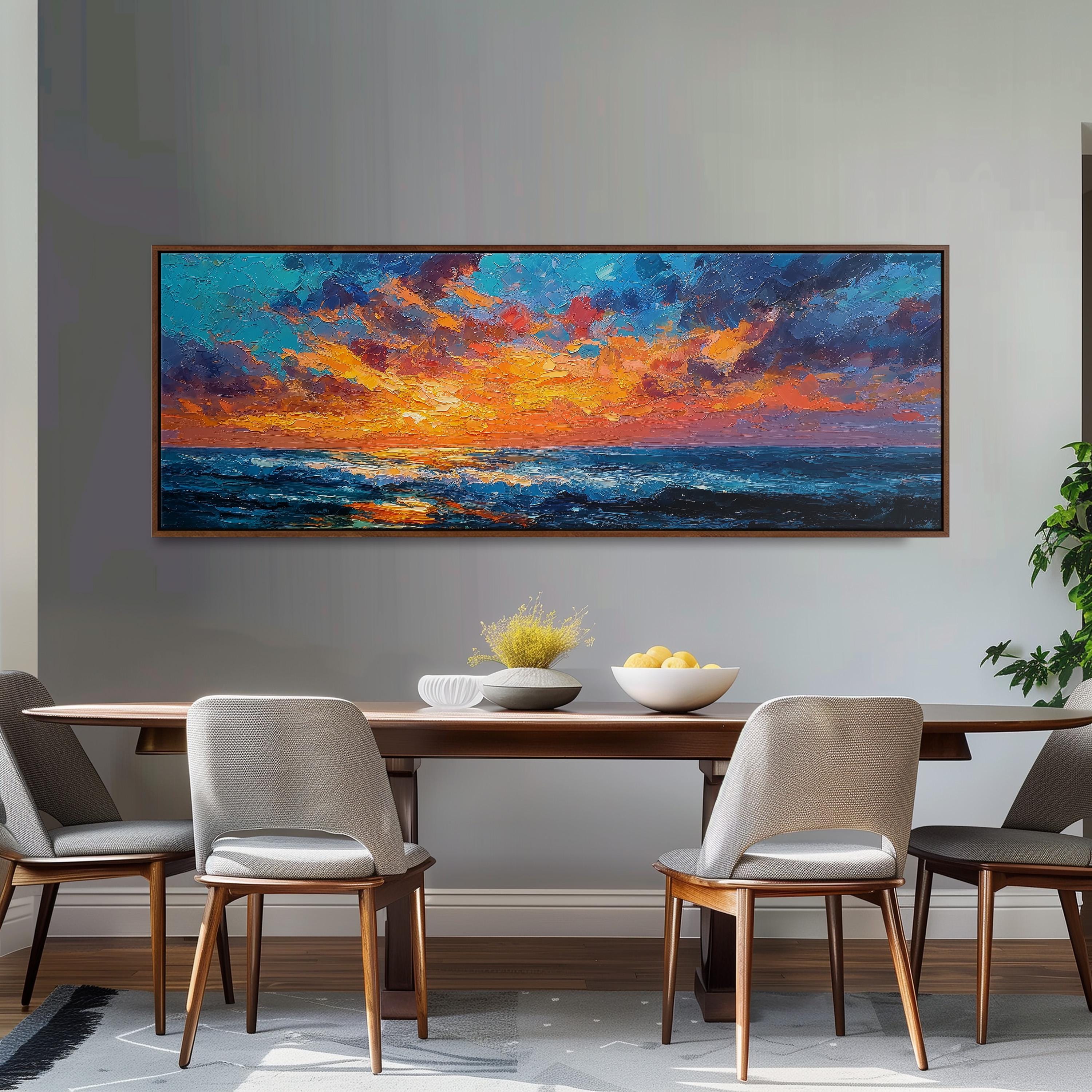 a dining room with a large painting of a sunset over the ocean hanging on the wall above a wooden dining table with four chairs. The table is set with a bowl of fruit and a vase of flowers, creating a cozy and inviting atmosphere.