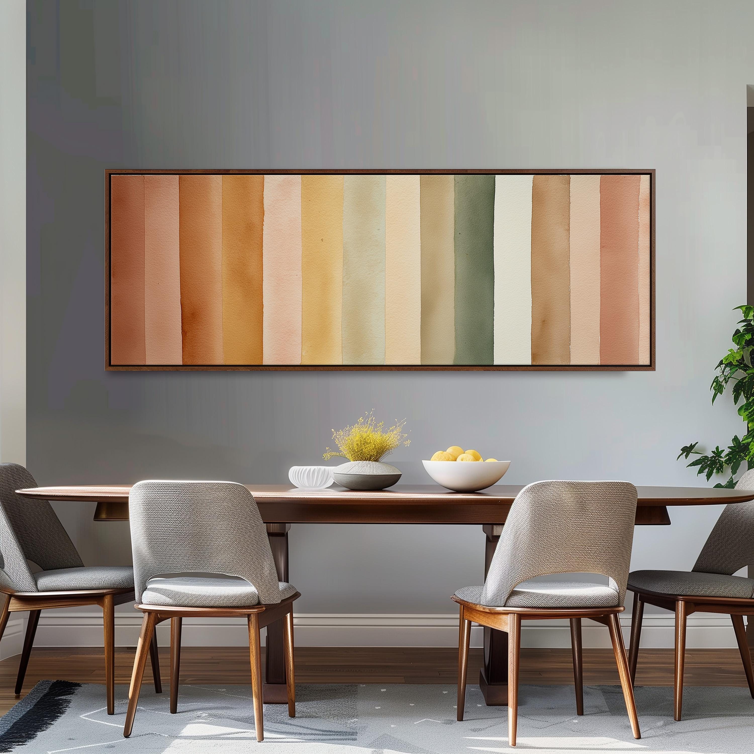 a dining room with a wooden table and four chairs. Above the table, there is a large painting with horizontal stripes in various shades of orange, yellow, green, and white. The painting is hanging on a gray wall. On the table, there is a bowl of fruit and a vase of flowers.