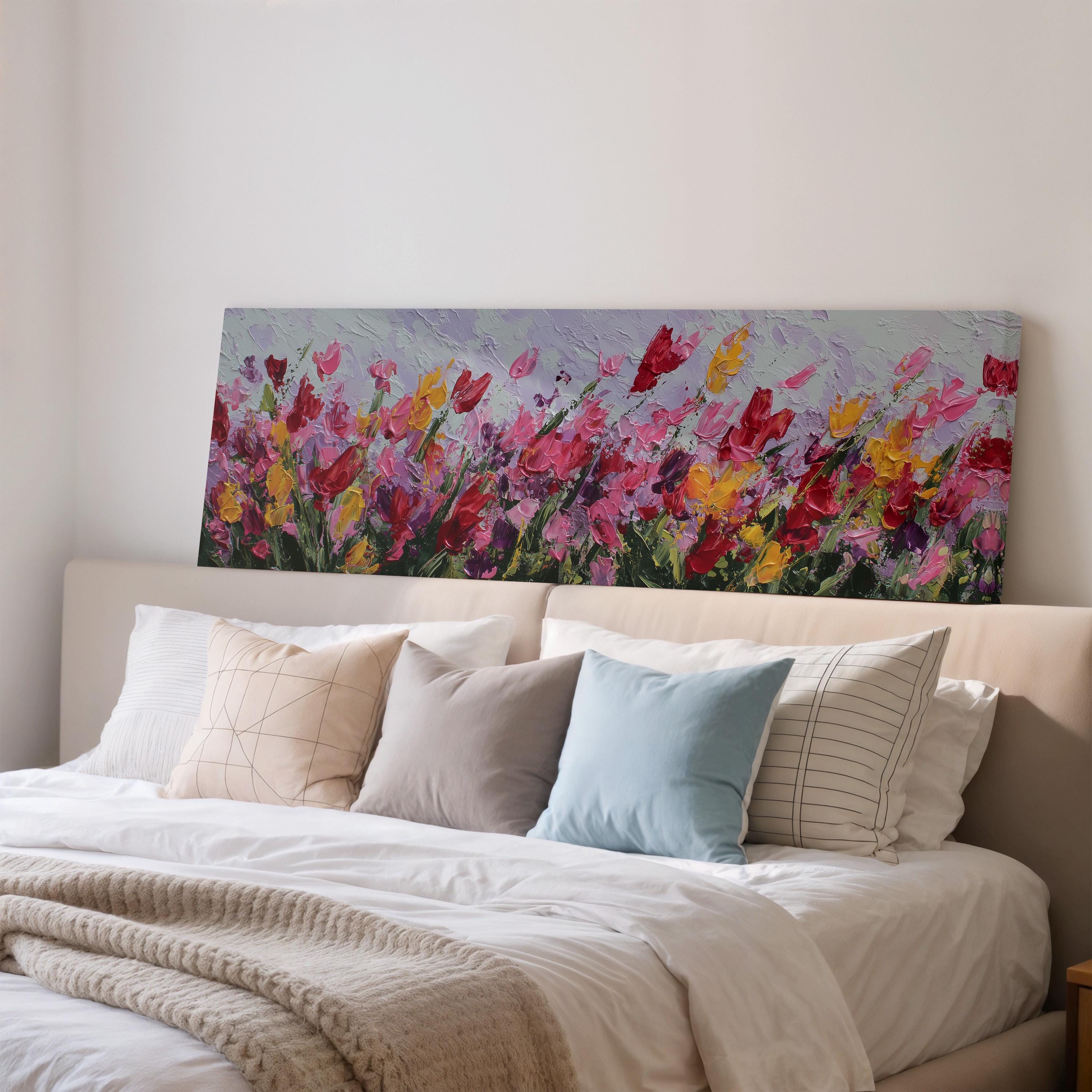 a large painting of a field of colorful flowers hanging above a bed with white pillows and a gray blanket.