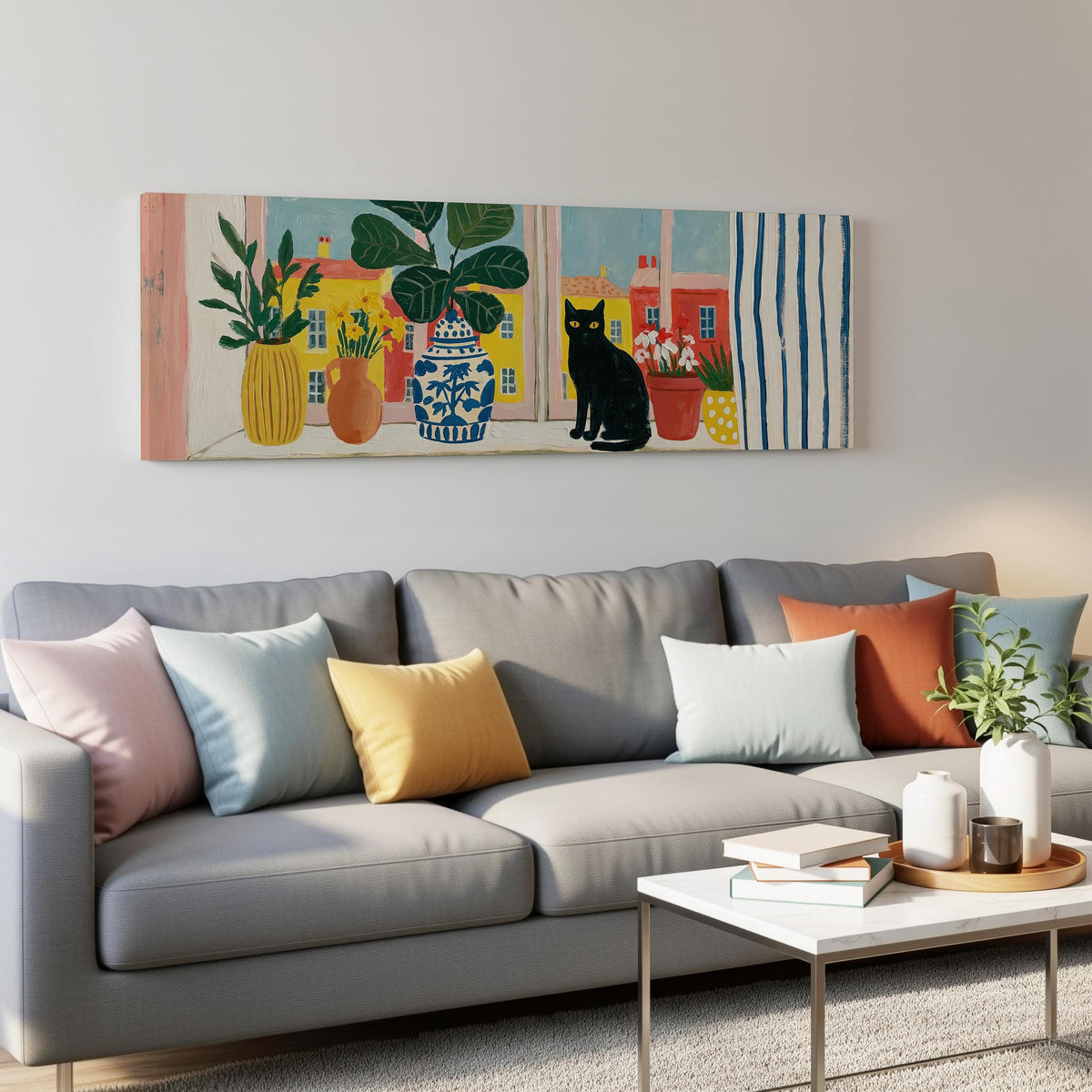 Black cat on a windowsill overlooking a colorful village panoramic canvas print above a grey sofa in a living room