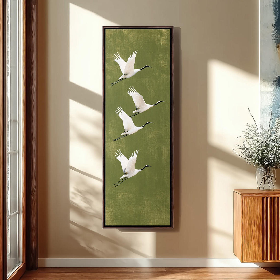 Four white cranes flying on olive green long vertical canvas print in a sunlit living space