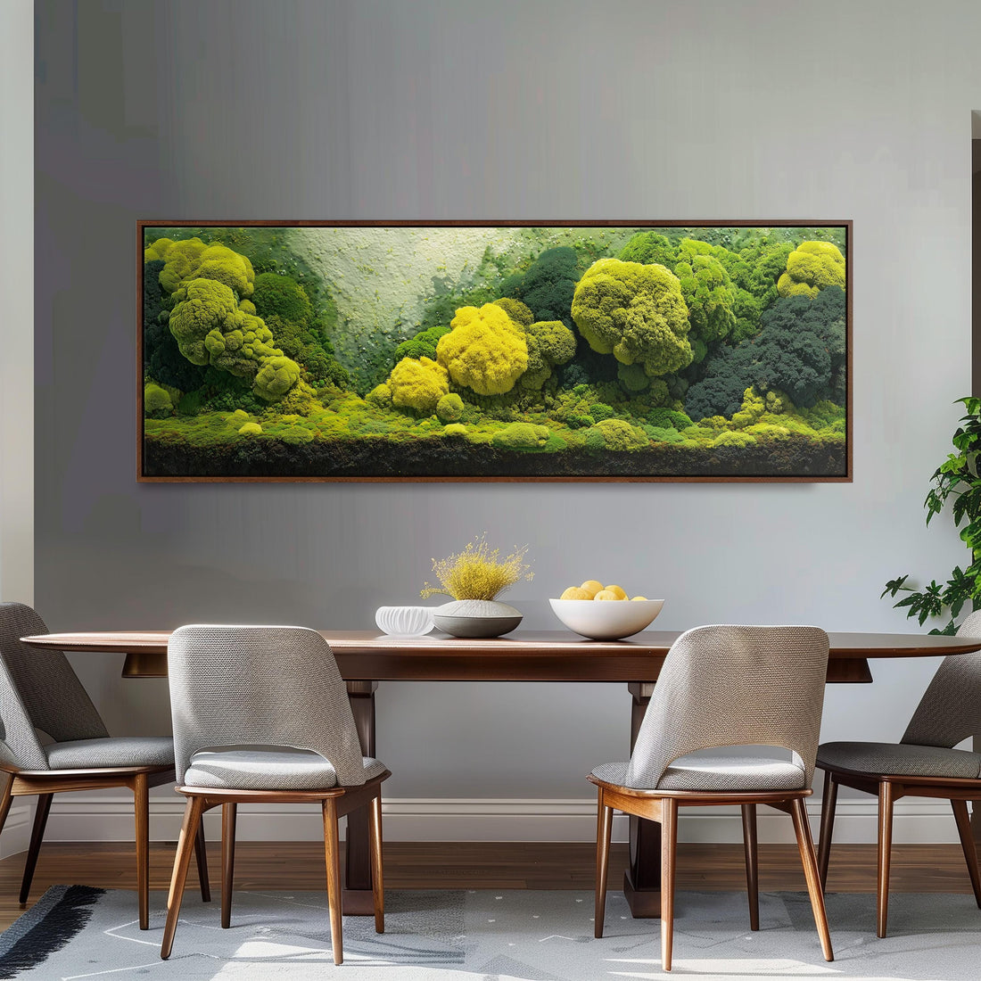 a dining room with a large, framed painting of a lush, green landscape hanging on the wall above a wooden dining table with four chairs. The table is set with a bowl of fruit and a vase of flowers, creating a cozy and inviting atmosphere.