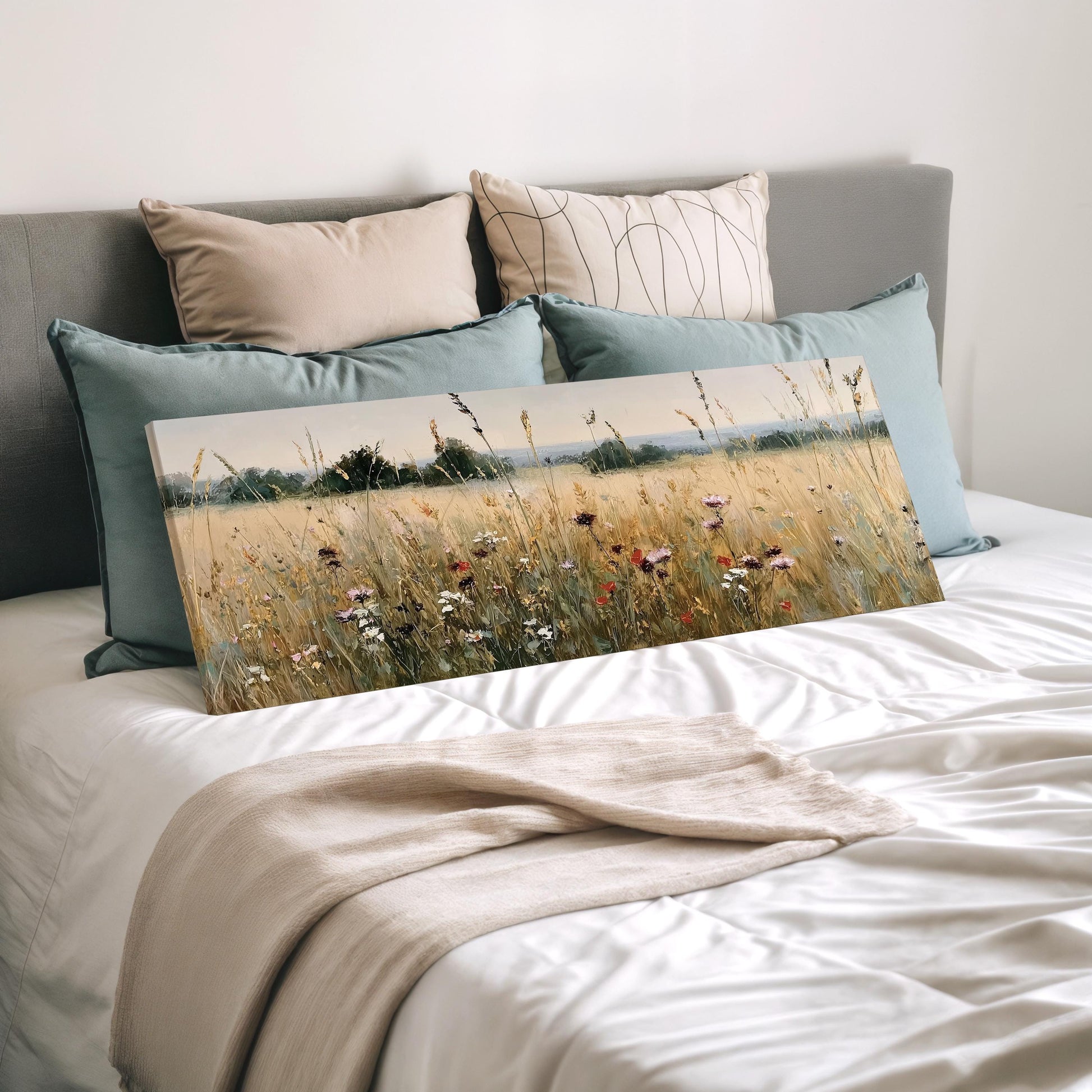 a bedroom with a bed and a painting of a field of flowers on it. The bed is covered with a white comforter and has several pillows on it. The painting is placed on the bed, and the bed is positioned against a wall.
