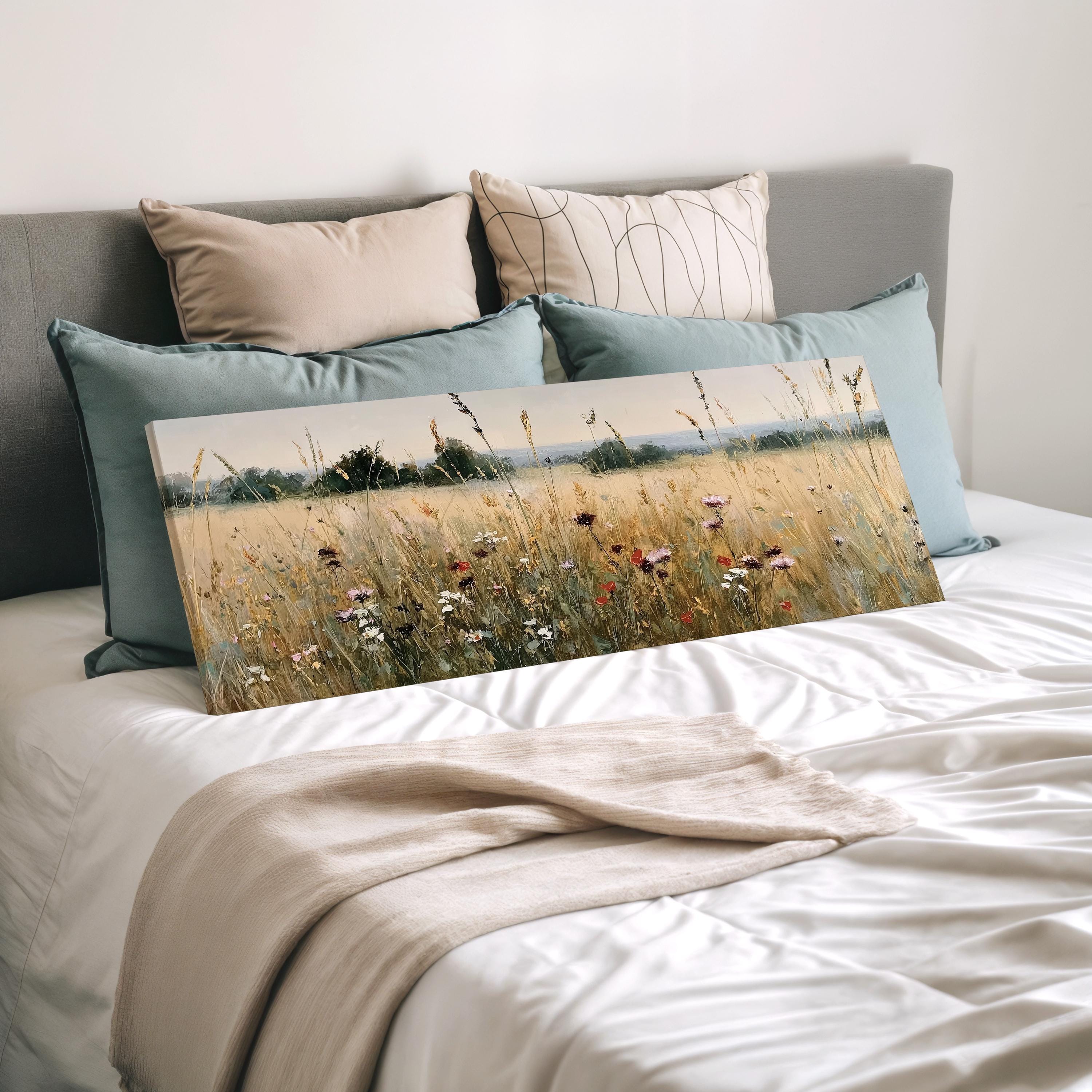 a bedroom with a bed and a painting of a field of flowers on it. The bed is covered with a white comforter and has several pillows on it. The painting is placed on the bed, and the bed is positioned against a wall.