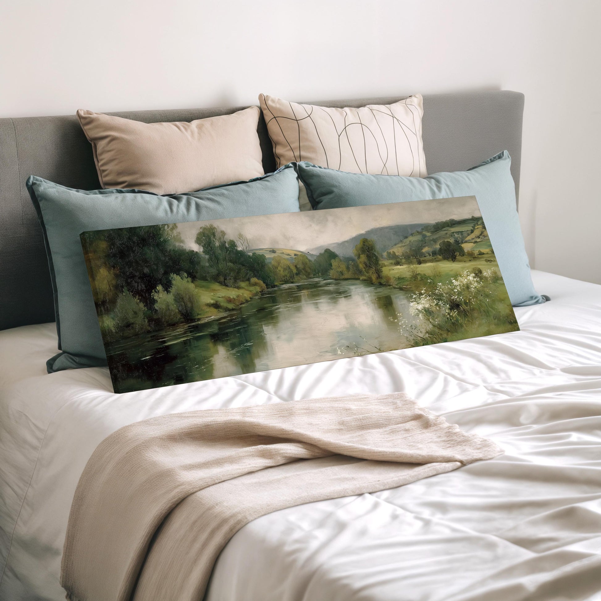 a painting of a serene landscape with a river and trees, displayed on a bed with a white comforter and pillows.