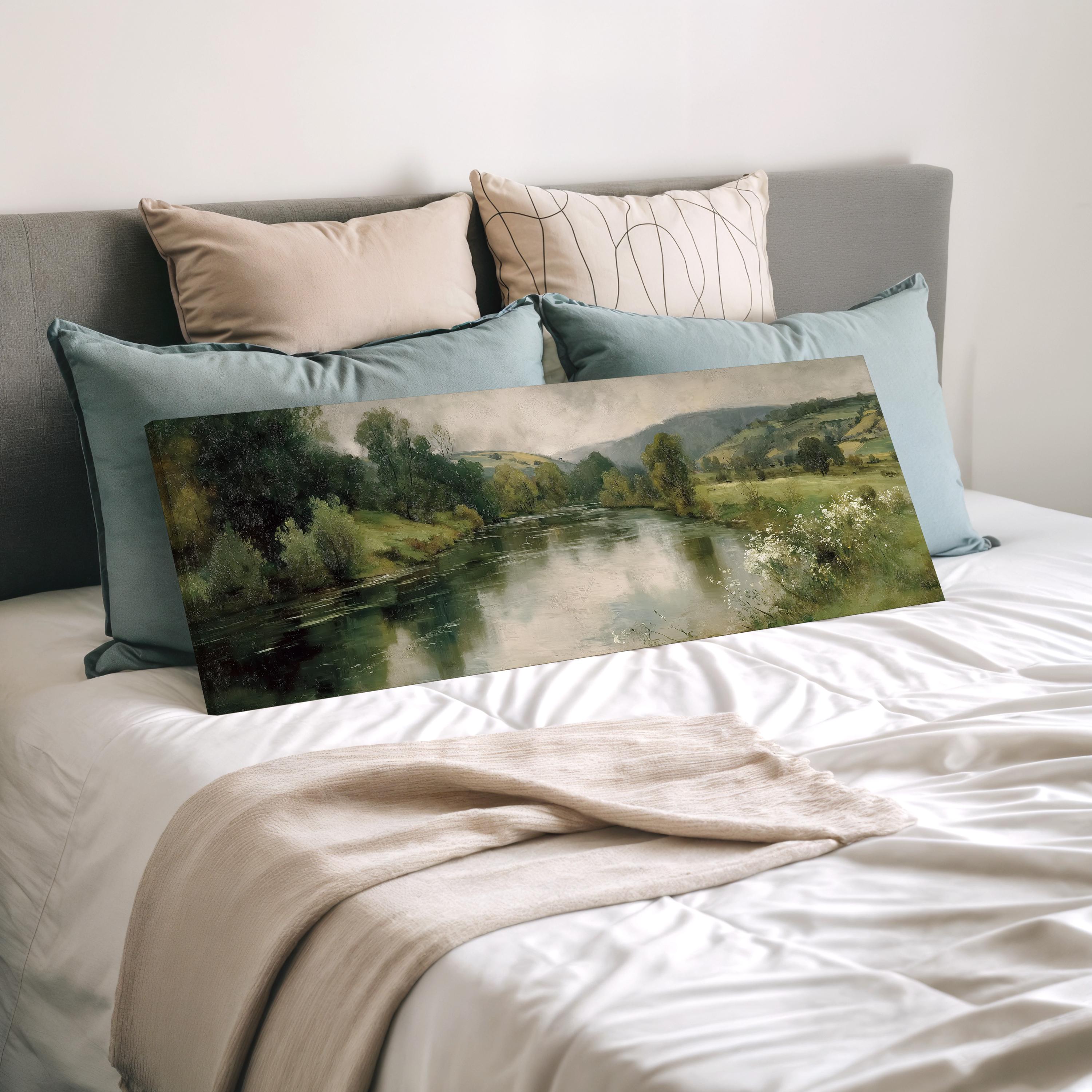a painting of a serene landscape with a river and trees, displayed on a bed with a white comforter and pillows.