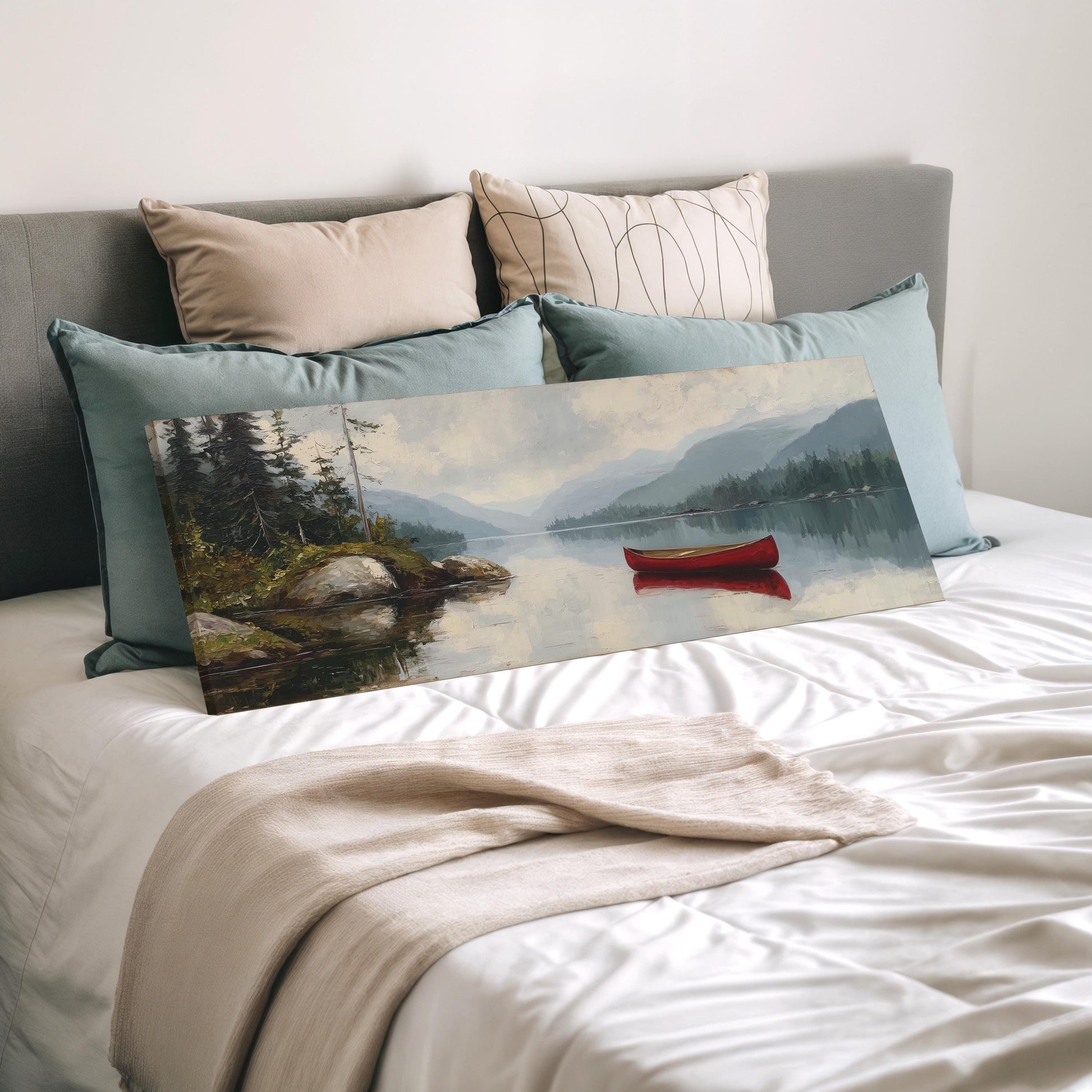 a bedroom with a large painting of a lake and a red canoe on the bed, surrounded by pillows and a blanket.