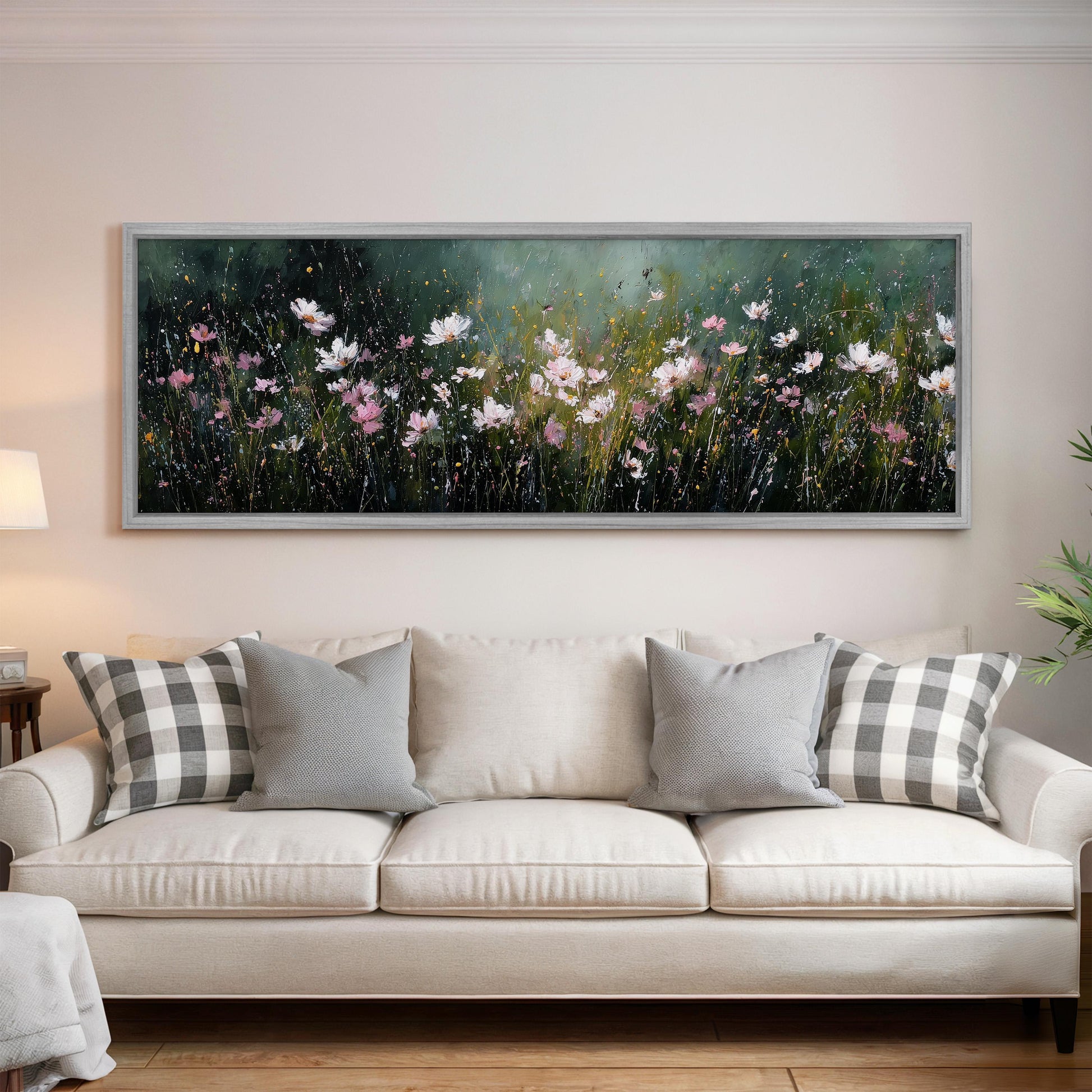 a large, framed painting of a field of flowers hanging on a wall above a white couch with gray and white plaid throw pillows.
