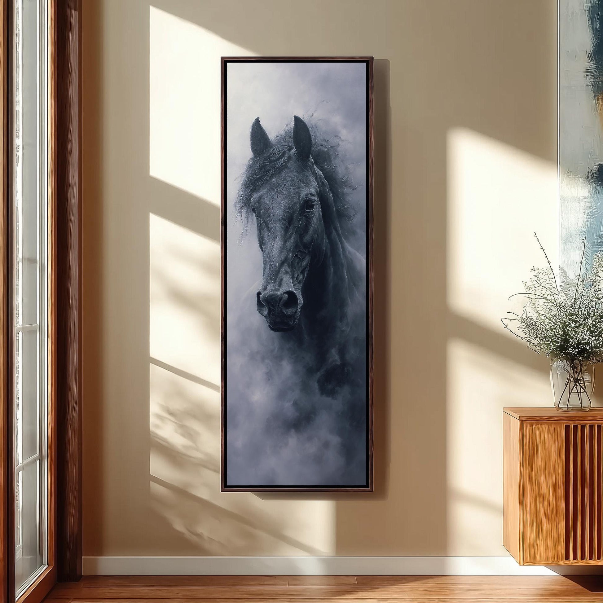 a large black horse in a dark frame, hanging on a wall in a room with a wooden cabinet and a vase of flowers.