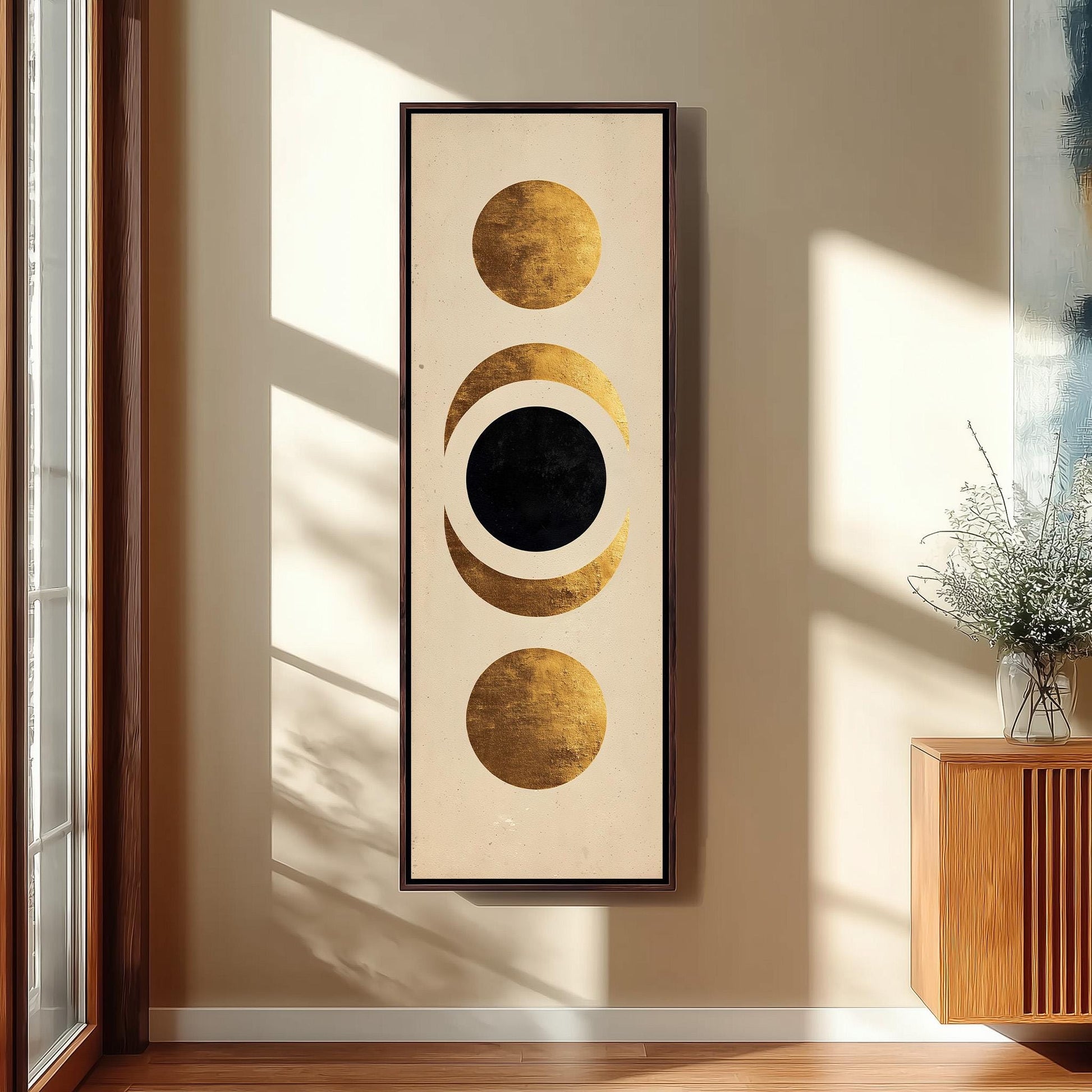 a large abstract painting hanging on a wall, with three circles and a black circle in the center. The painting is framed in black and has a gold border. The painting is placed next to a wooden cabinet and a vase of flowers, creating a visually appealing display.