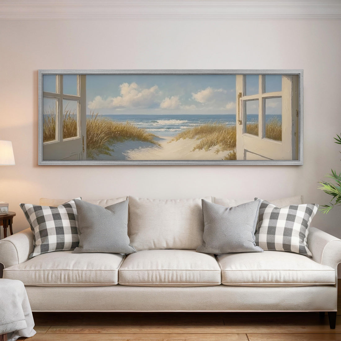 a large framed painting of a beach scene with open windows, hanging above a white sofa with gray and white pillows.